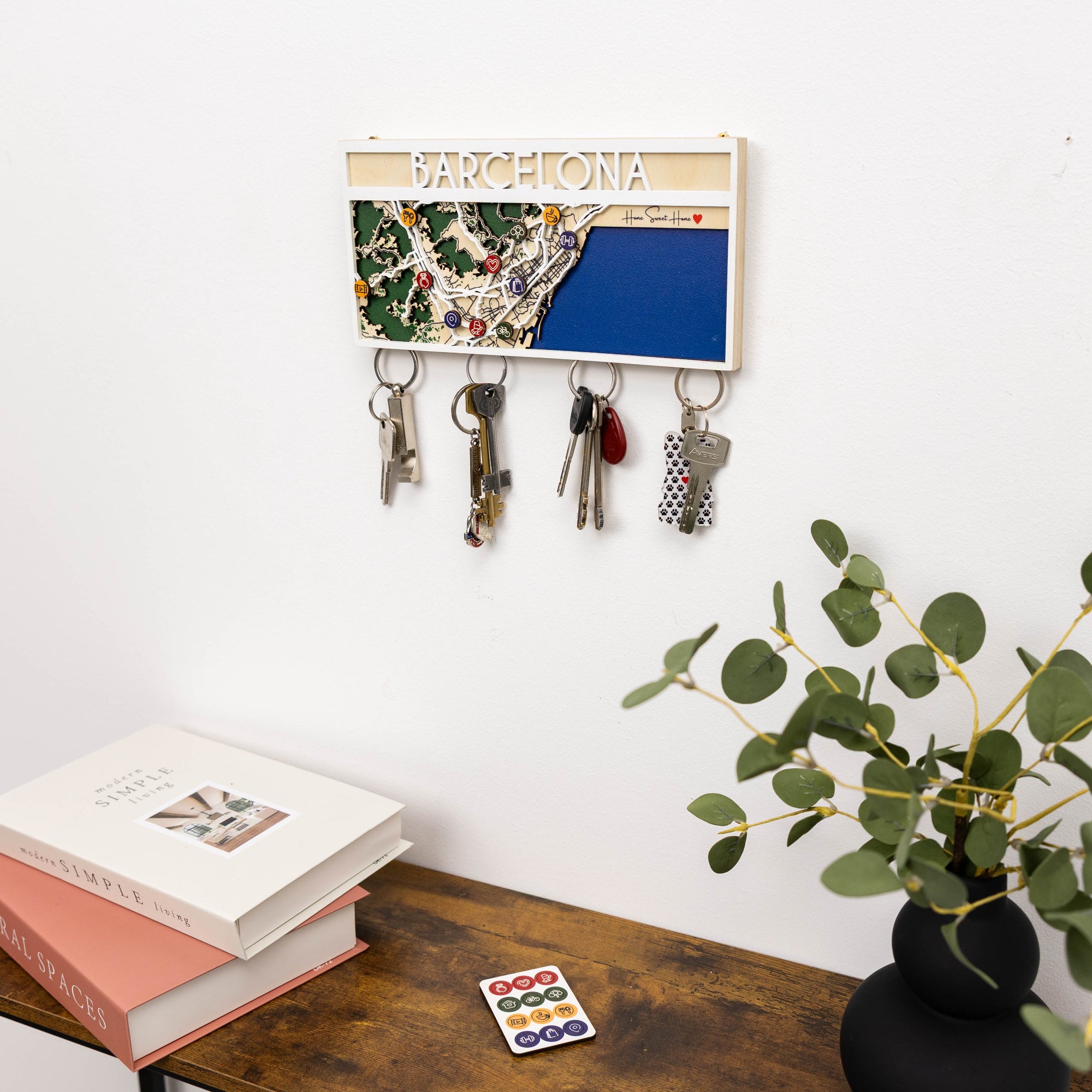 Key holder with keys on a wall above a desk with books and a plant.