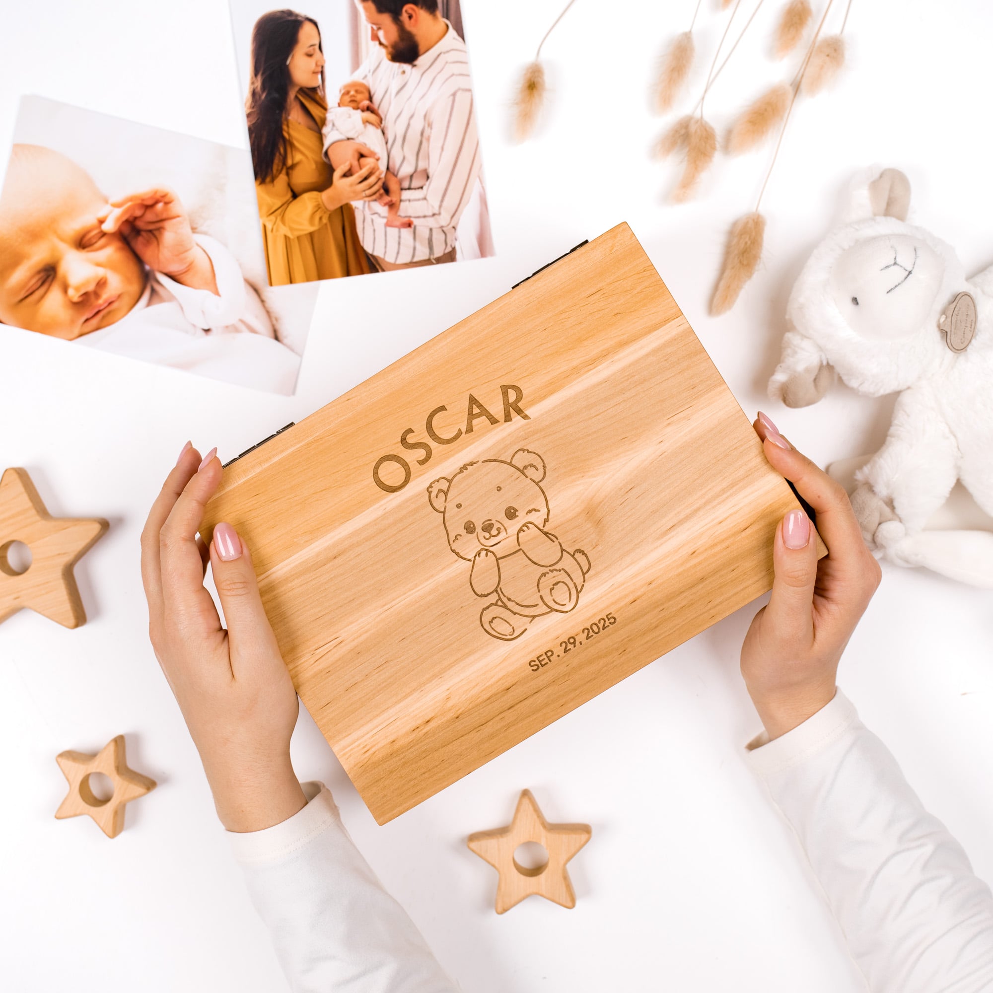 Wooden box engraved with 'OSCAR' and a teddy bear design, held by hands on a white surface with photos and toys.