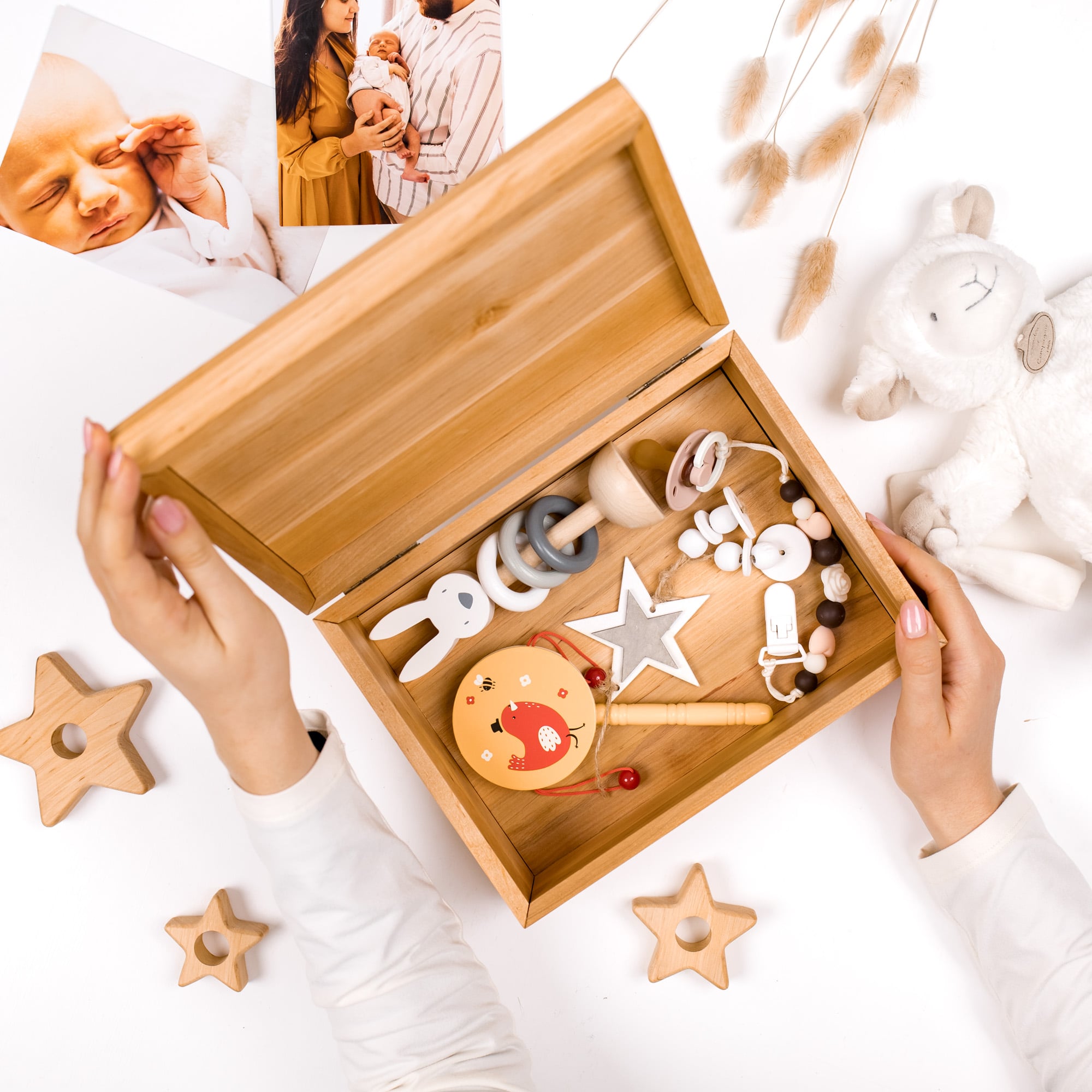 Wooden baby toy box with toys on a white surface, surrounded by baby items.
