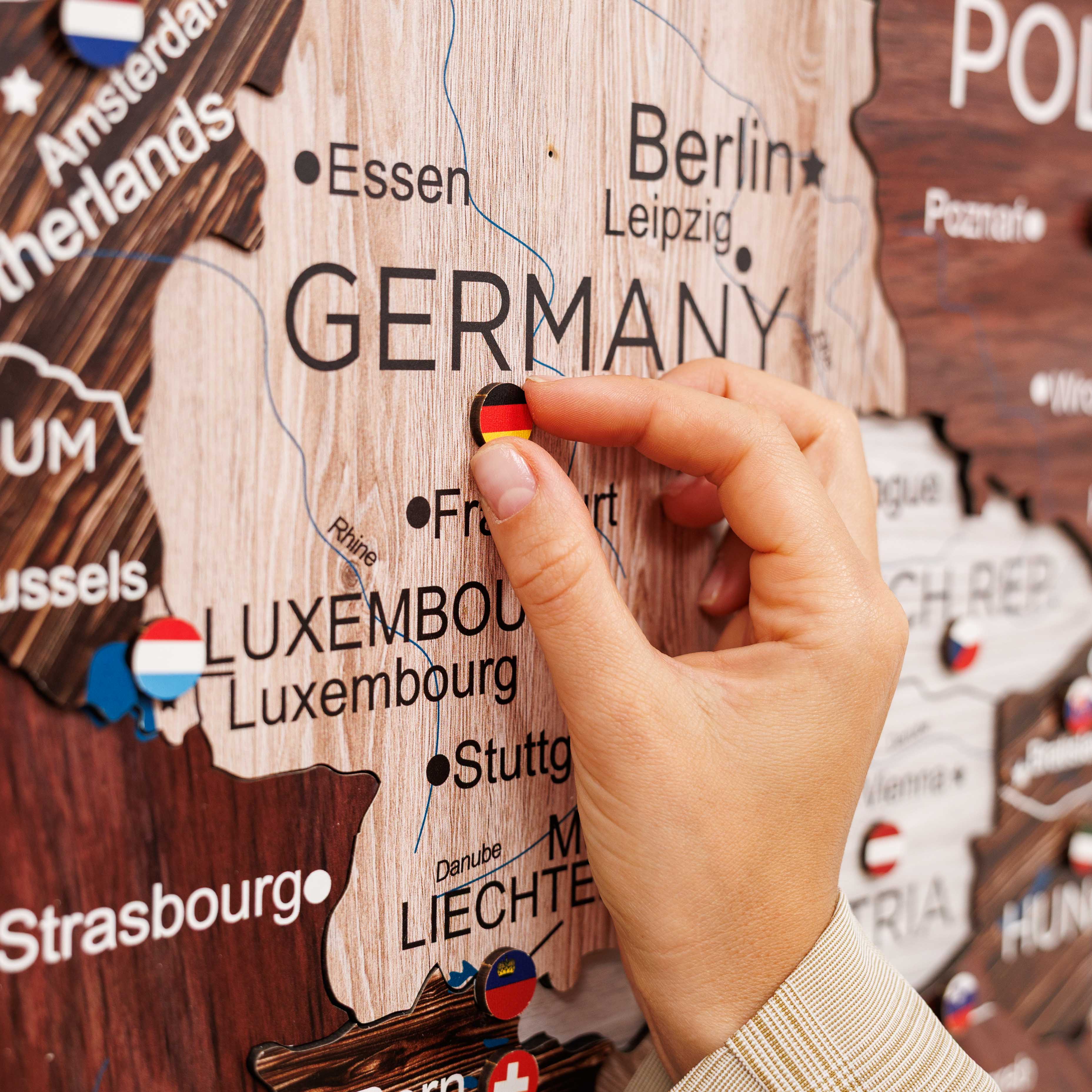 Hand placing a small flag on a wooden map of Europe, focusing on Germany.