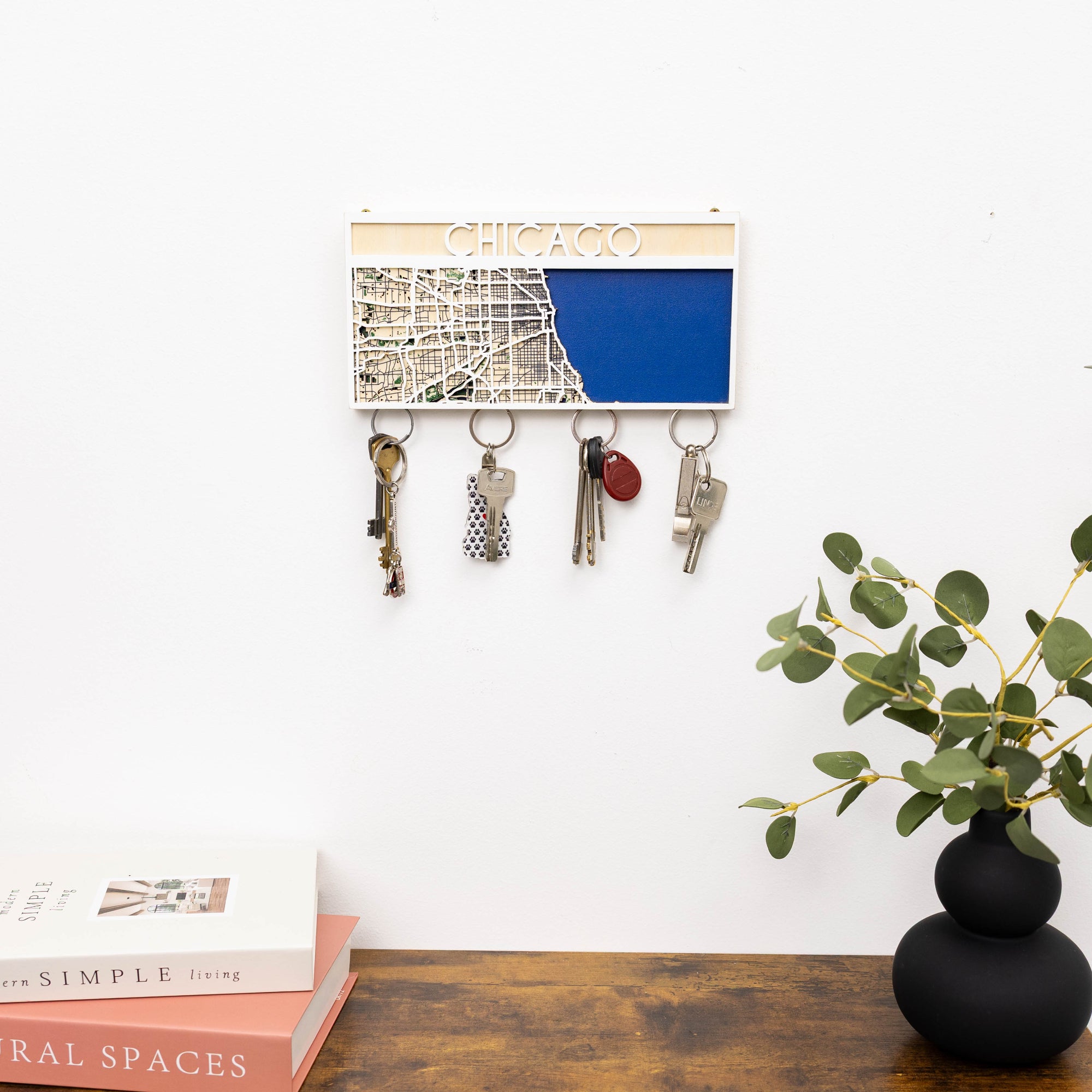 Key holder with keys attached on a wall next to a vase with greenery