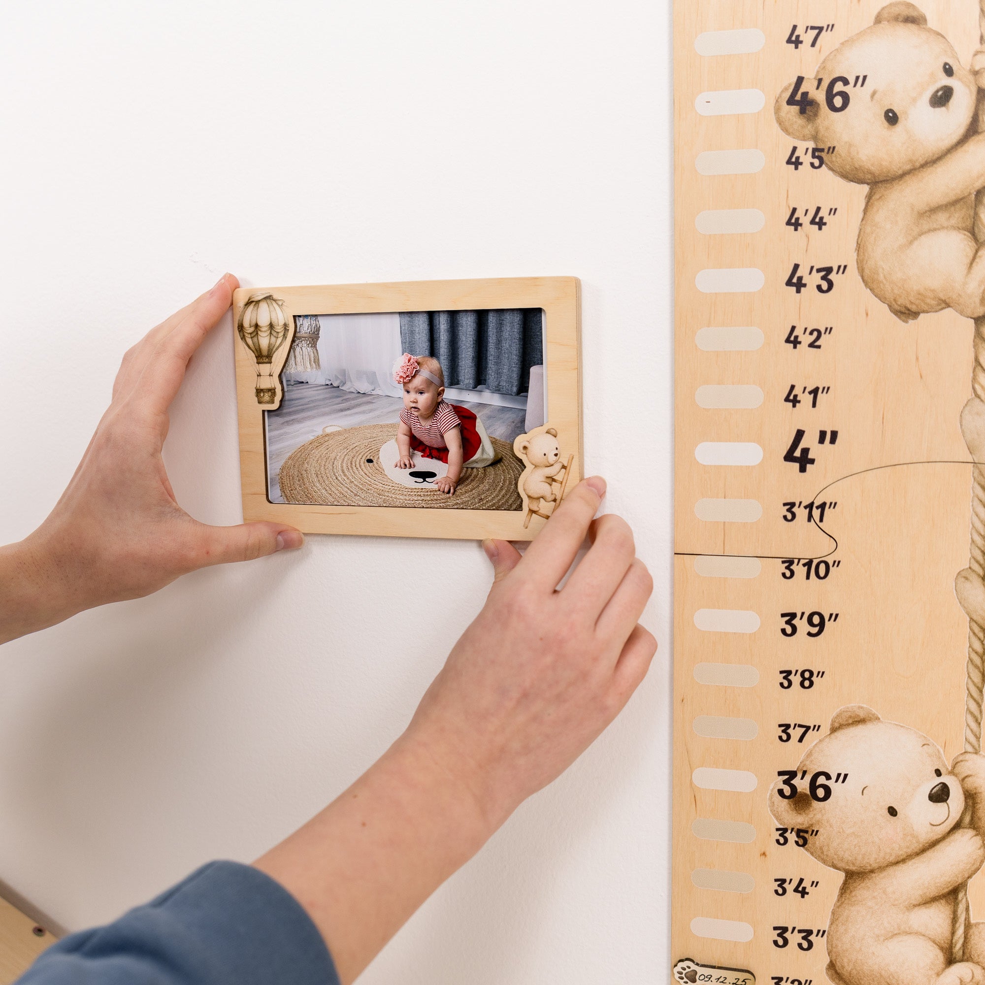 Person placing a photo frame on a wooden height chart with teddy bear designs.