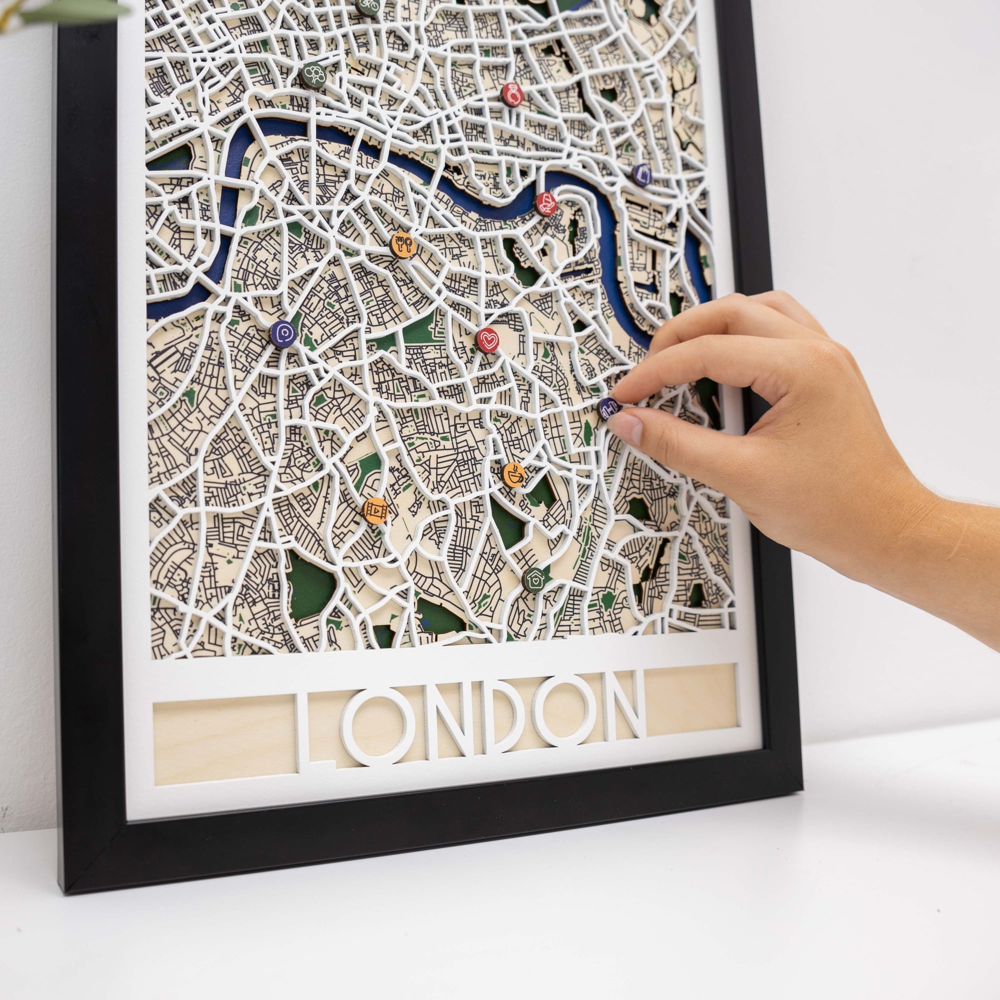 Framed map of London with decorative pins, held by a hand.
