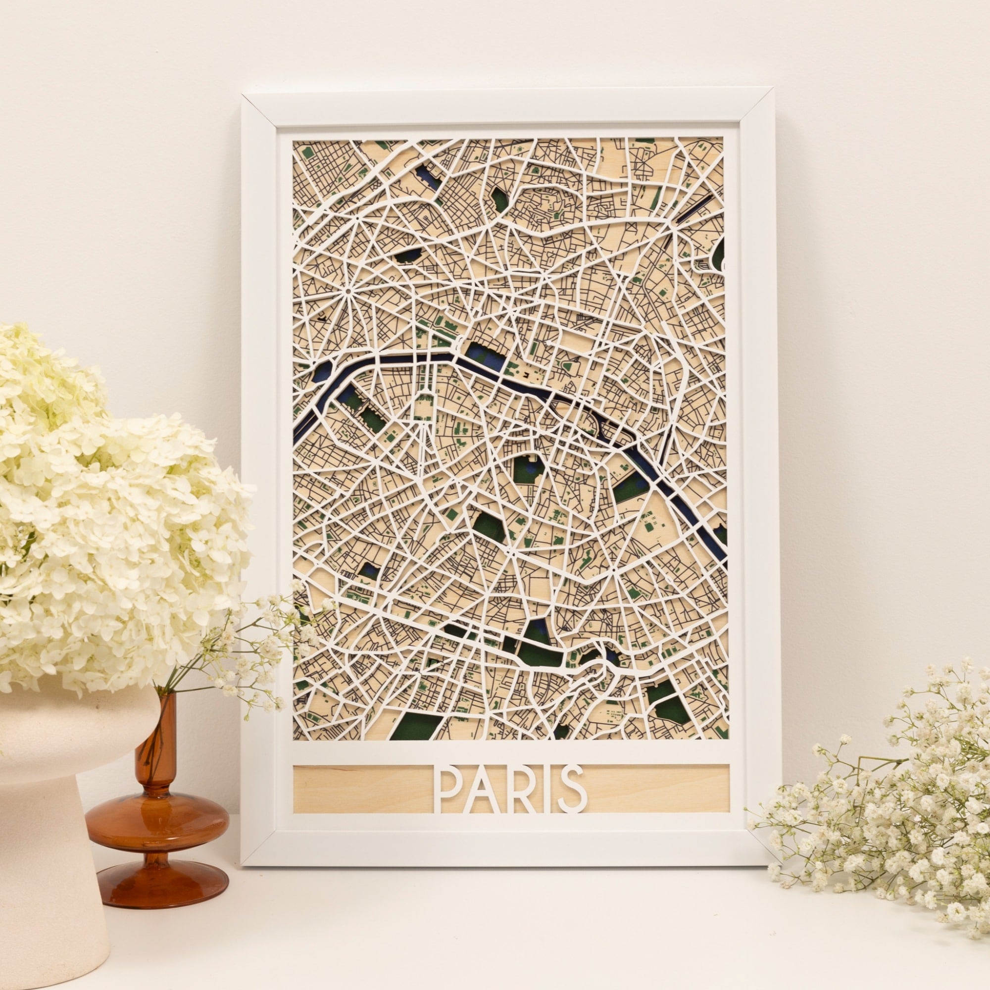 Framed map of Paris on a white wall with decorative flowers.