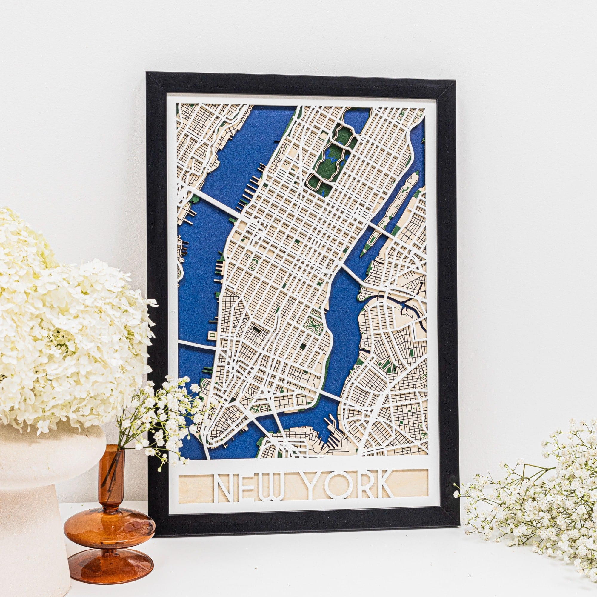 Framed map of New York City on a white wall with decorative flowers.