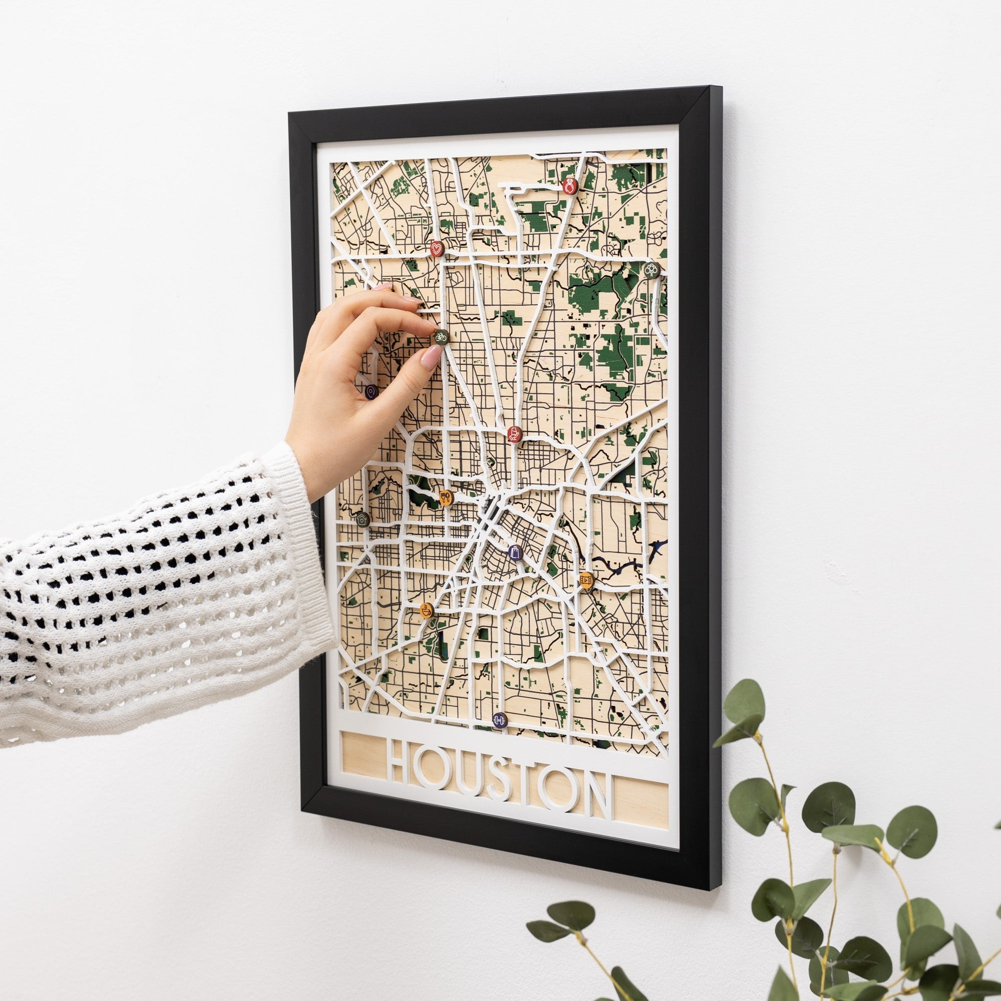 Framed map of Houston on a white wall with a hand reaching towards it.
