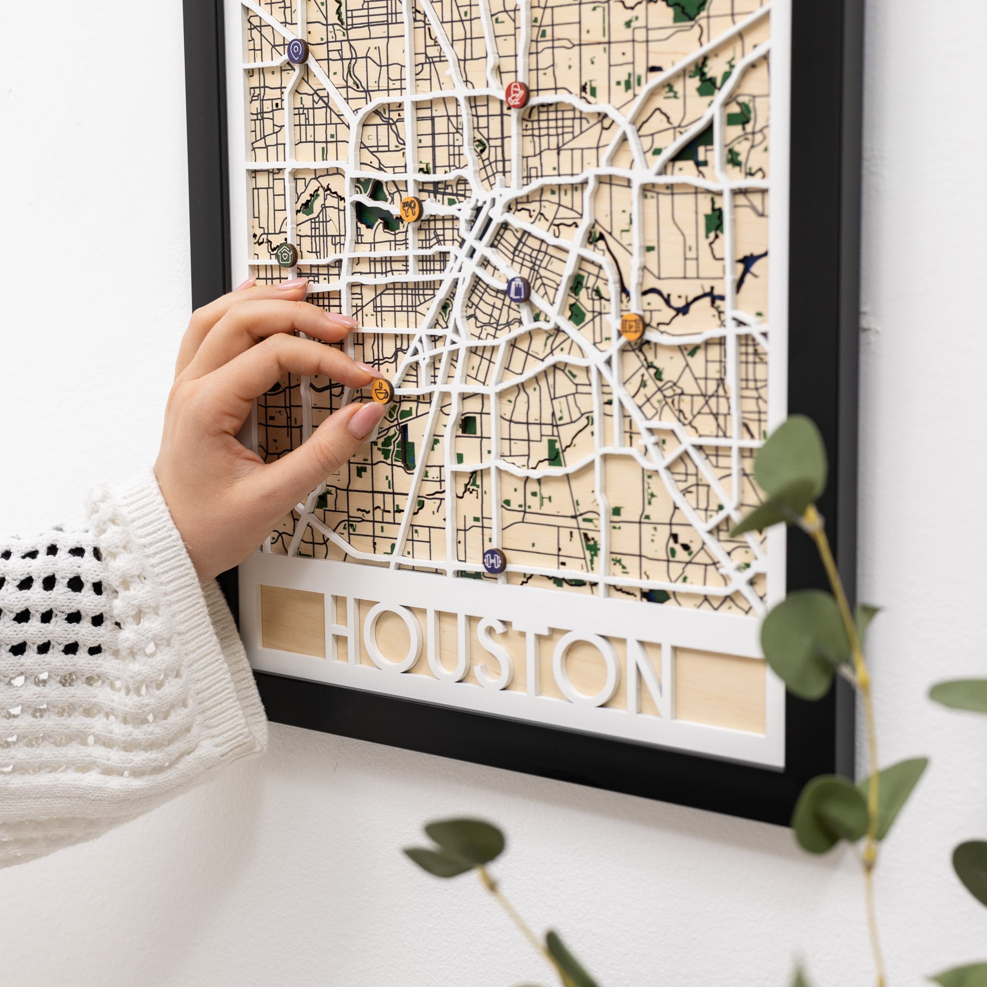 Hand placing a pin on a wooden map of Houston with decorative elements.