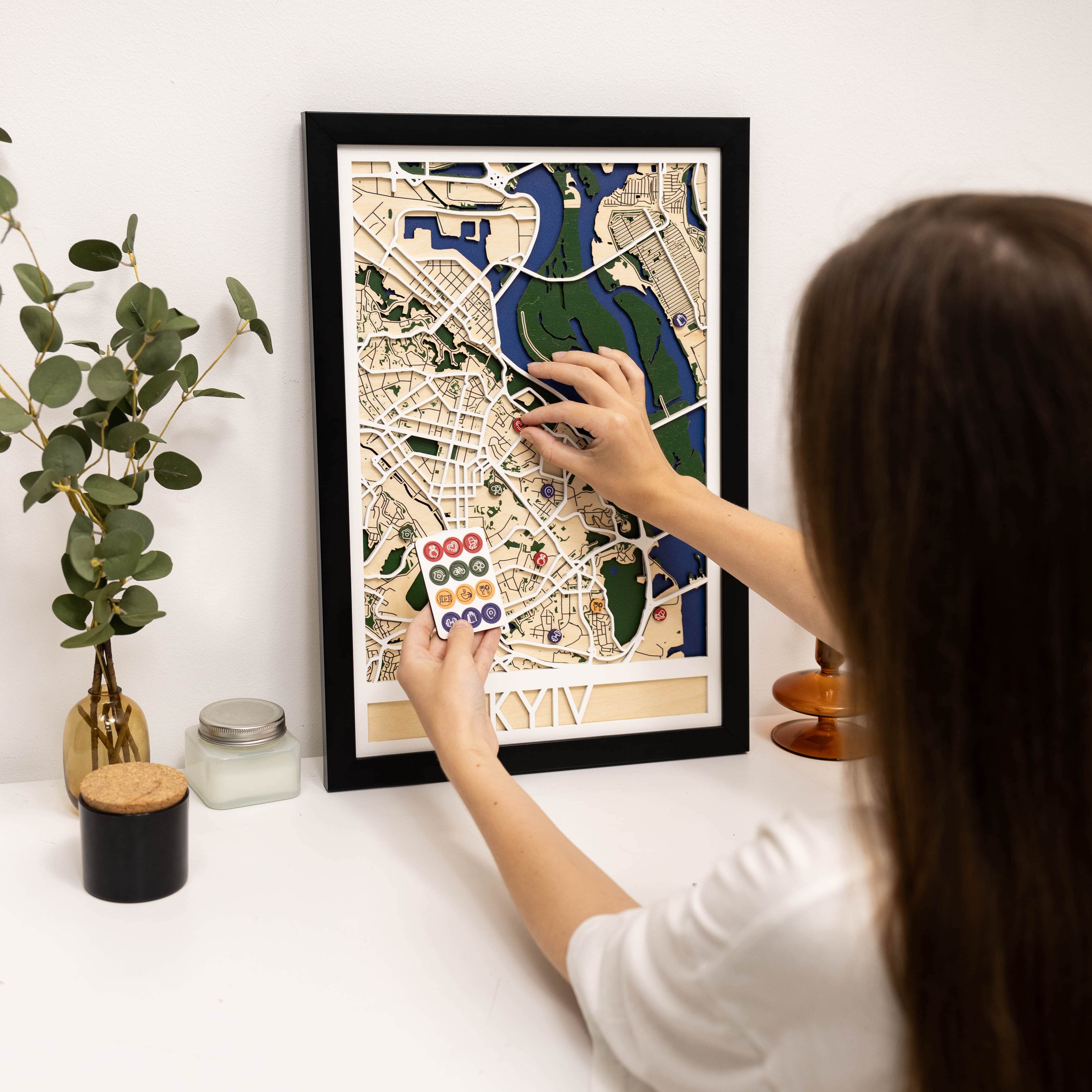 Person interacting with a framed map of Kyiv on a white surface.