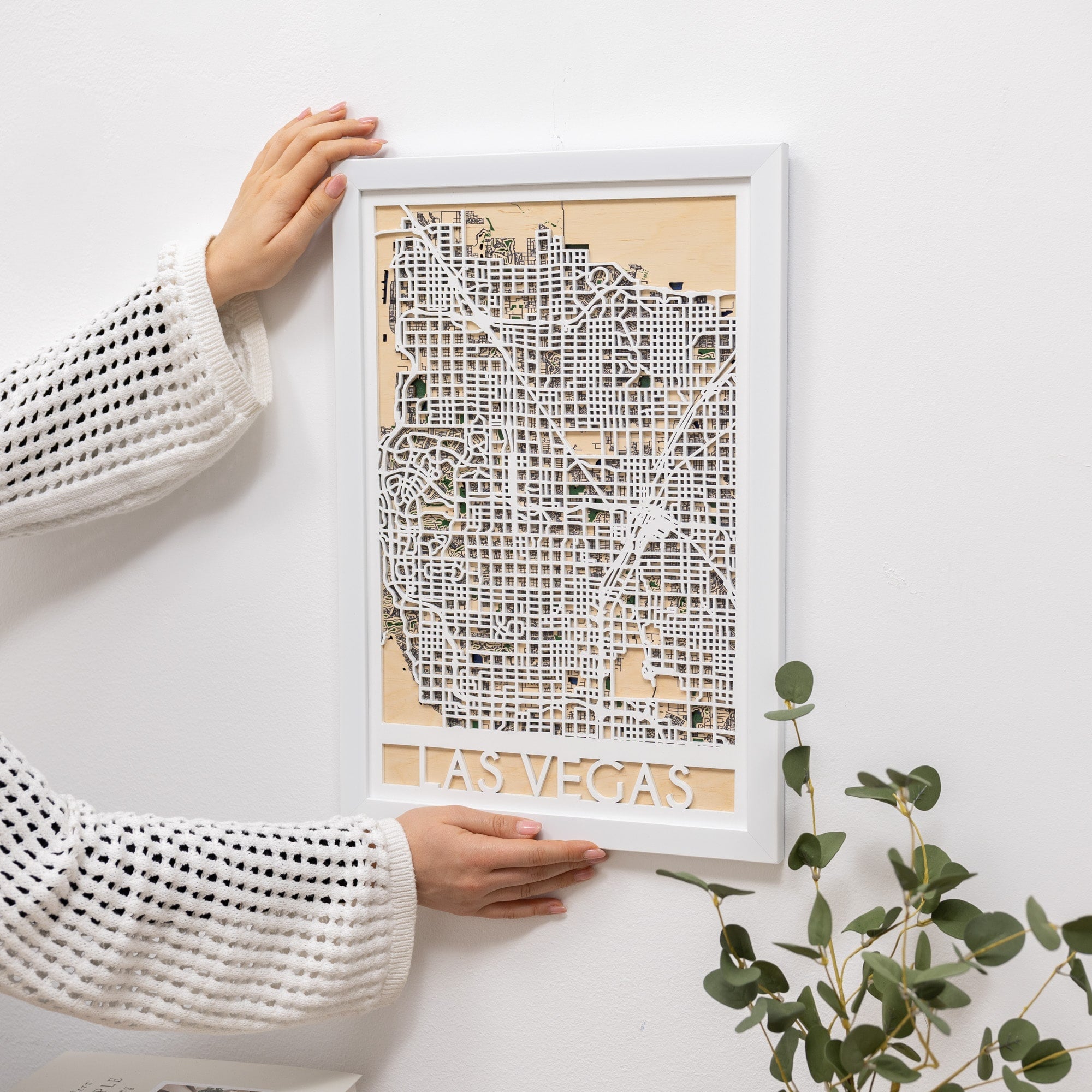 Framed map of Las Vegas held by a person on a white surface with a plant.