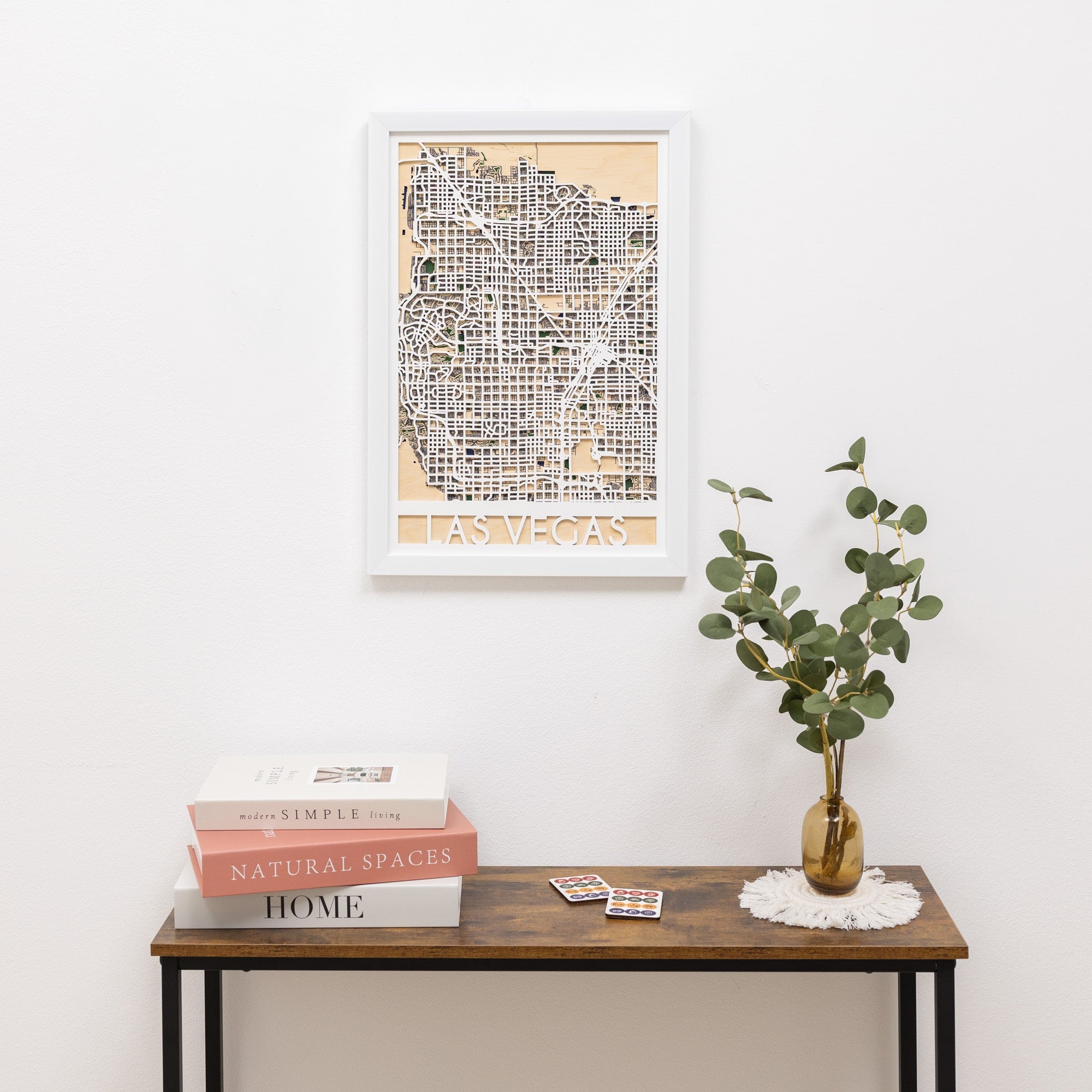 Framed Las Vegas map on a wall above a wooden table with books and a plant.