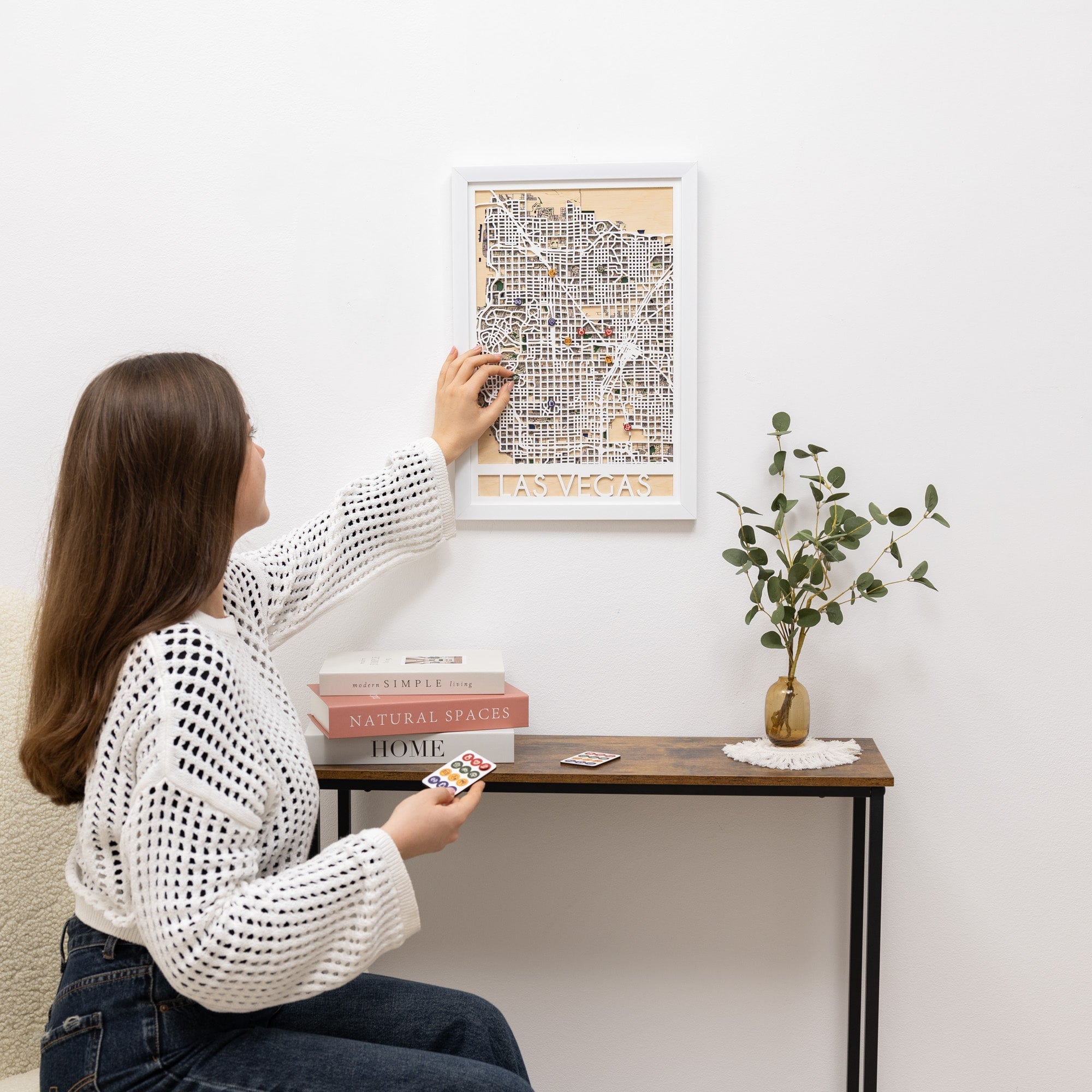 Woman hanging a framed map on a wall next to a small table with decor items.