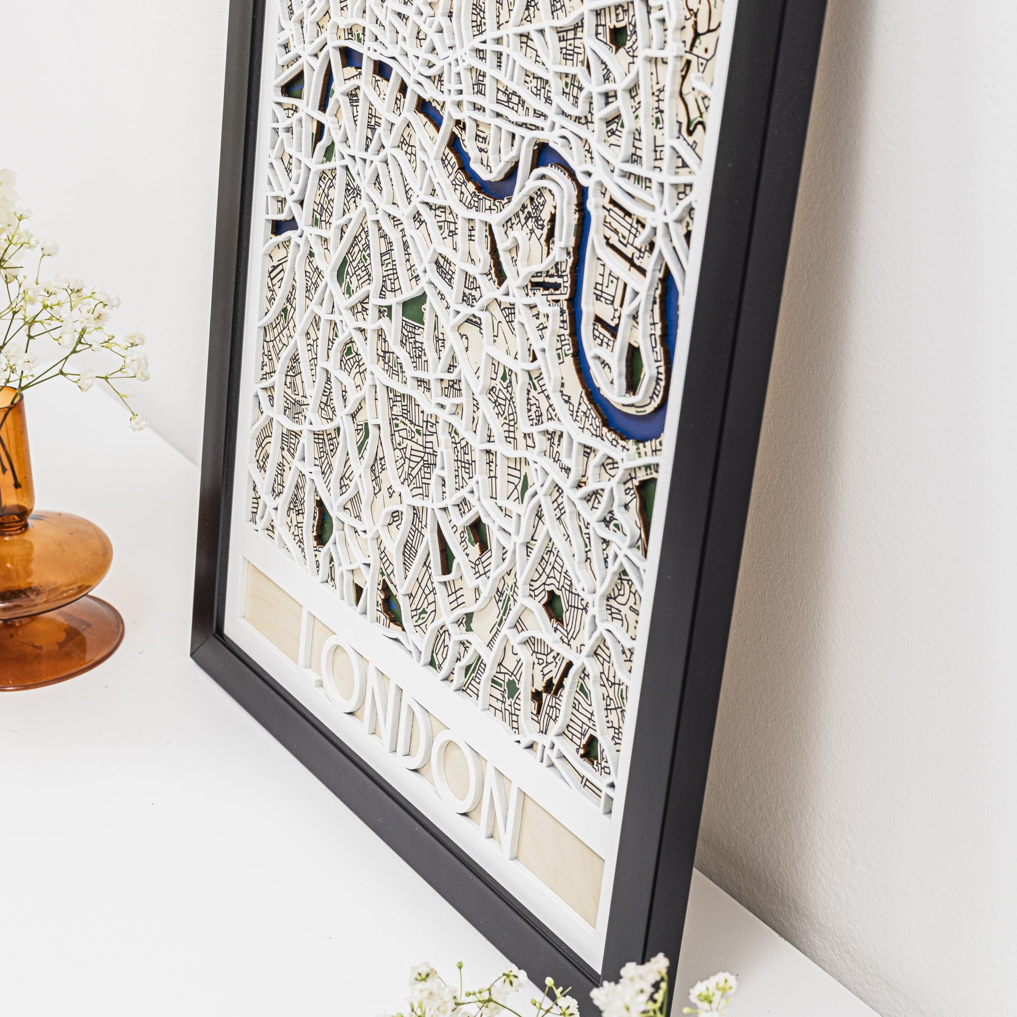 Framed map of London on a white surface with a vase and flowers in the background