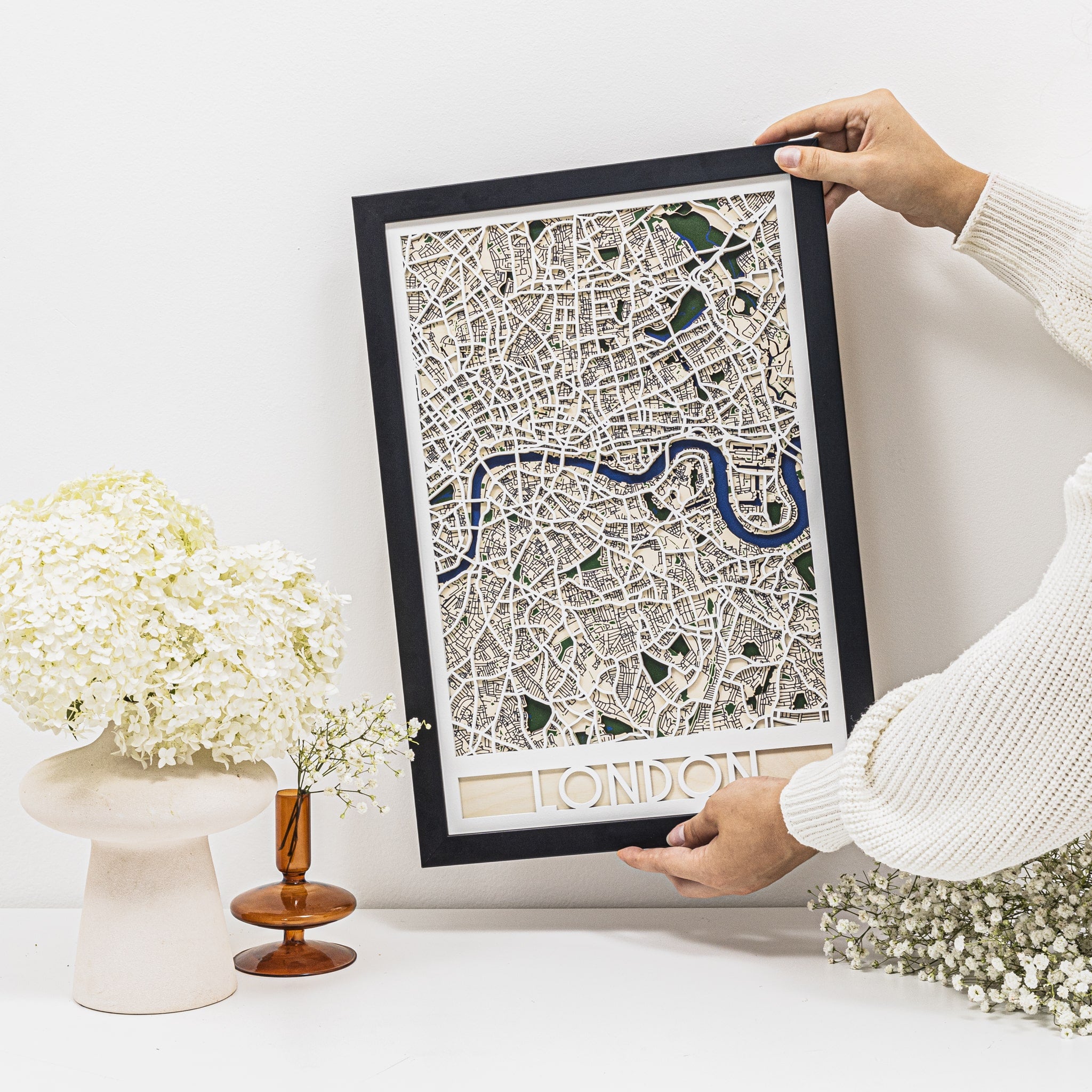Framed map of London held by a person with decorative elements in the background