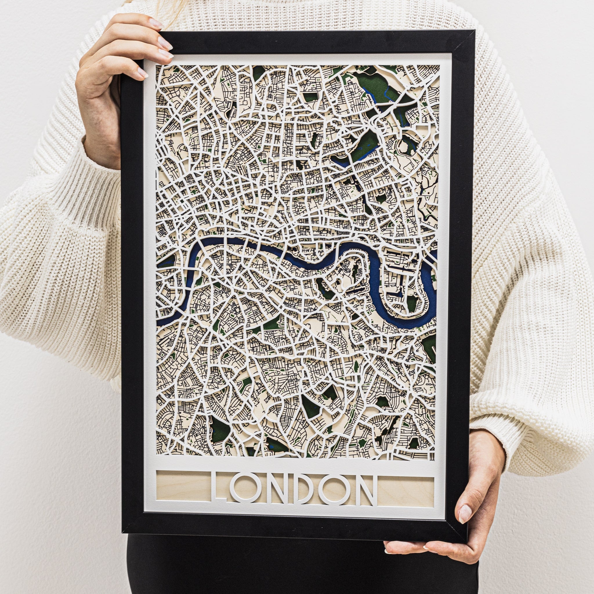 Framed map of London held by a person wearing a white sweater.