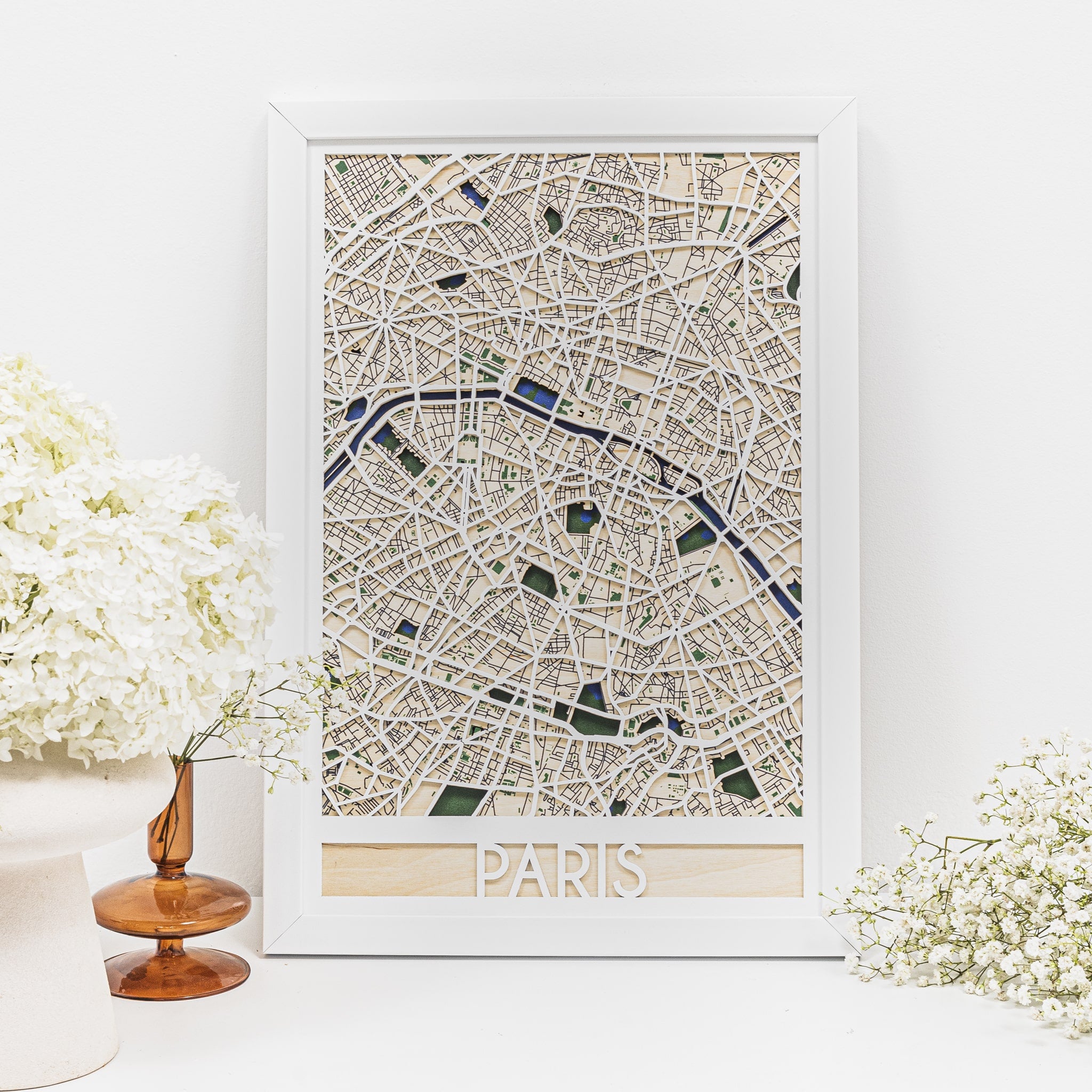 Framed map of Paris on a white wall with decorative flowers.