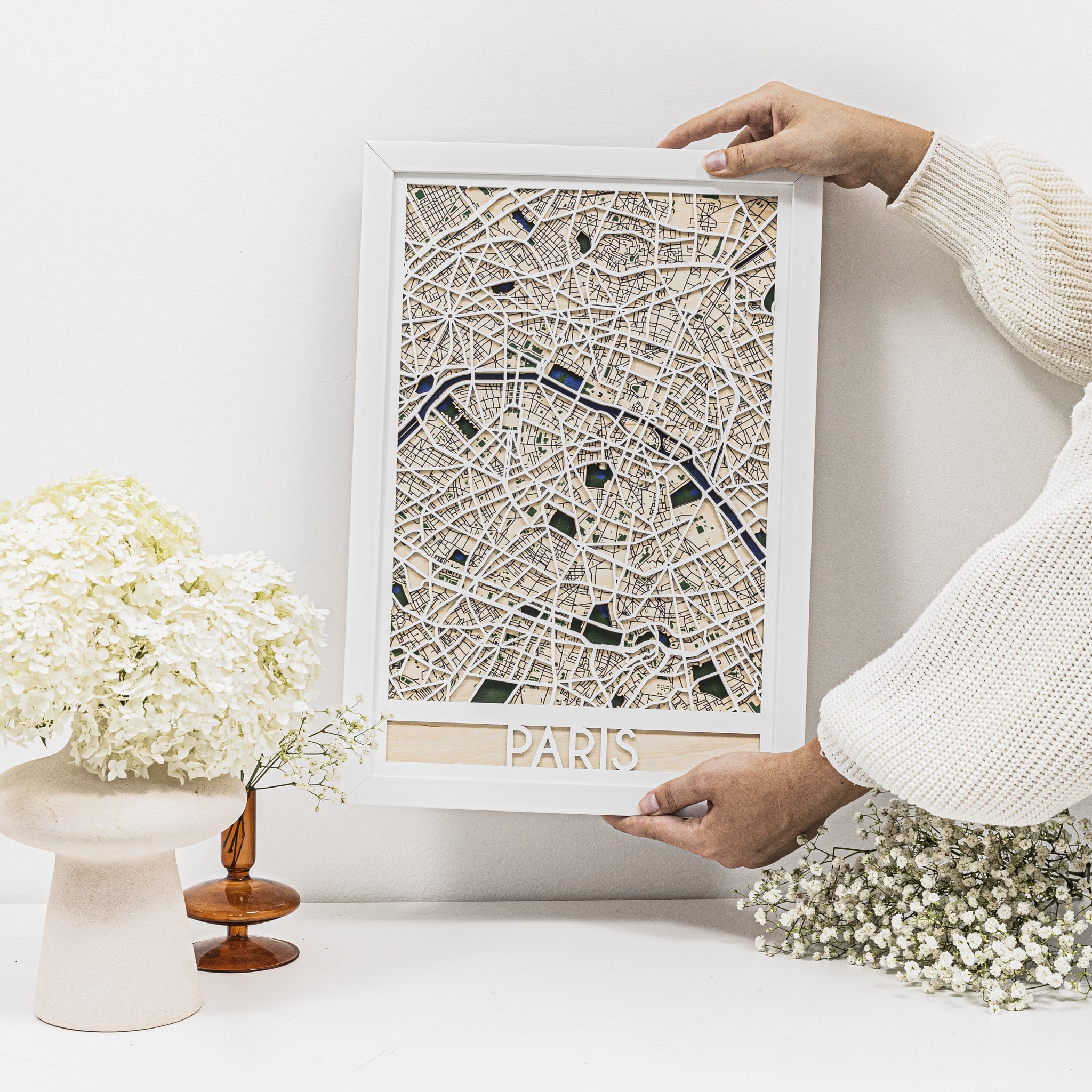 Person holding a framed map of Paris on a white surface with decorative elements.