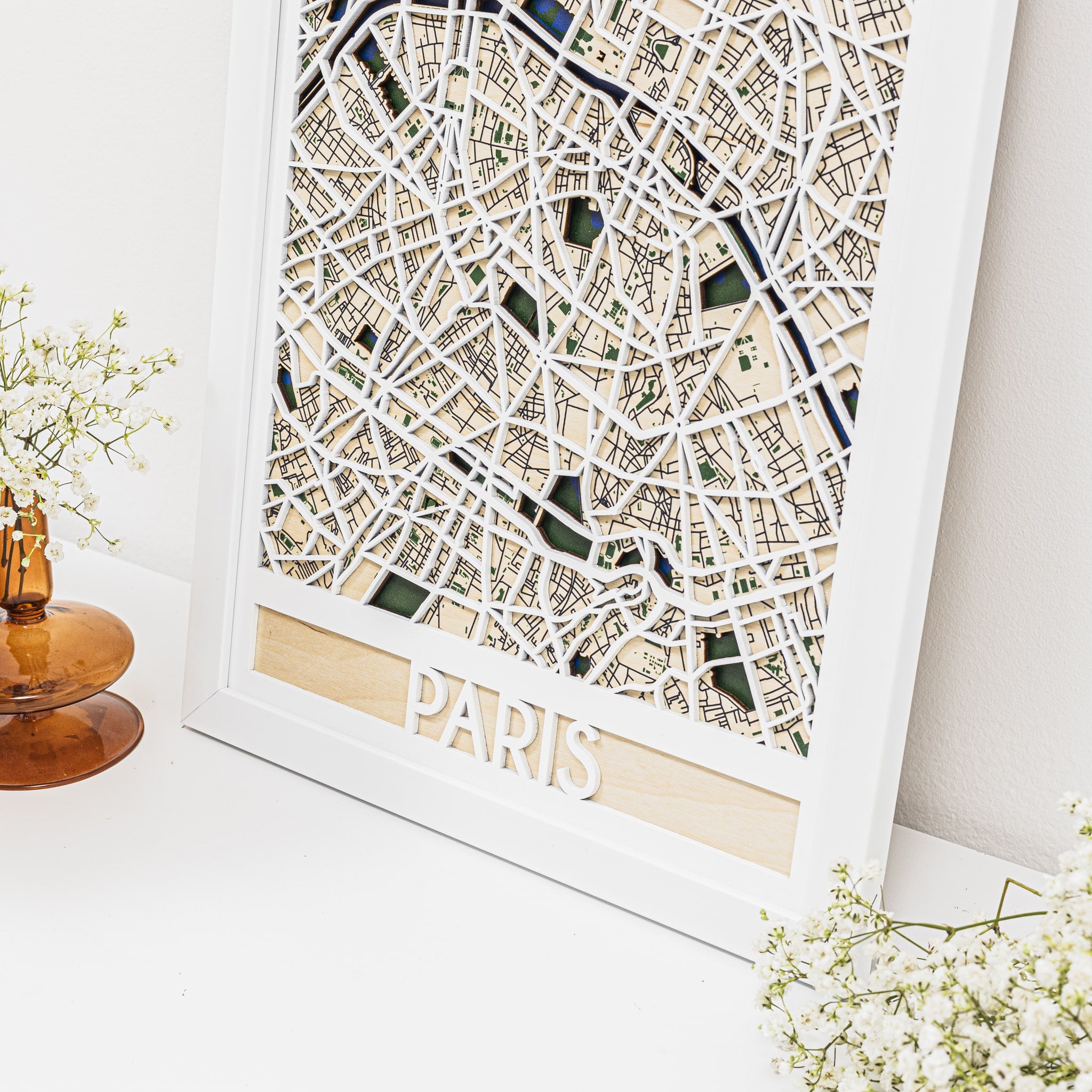 Framed map of Paris on a white surface with decorative elements.