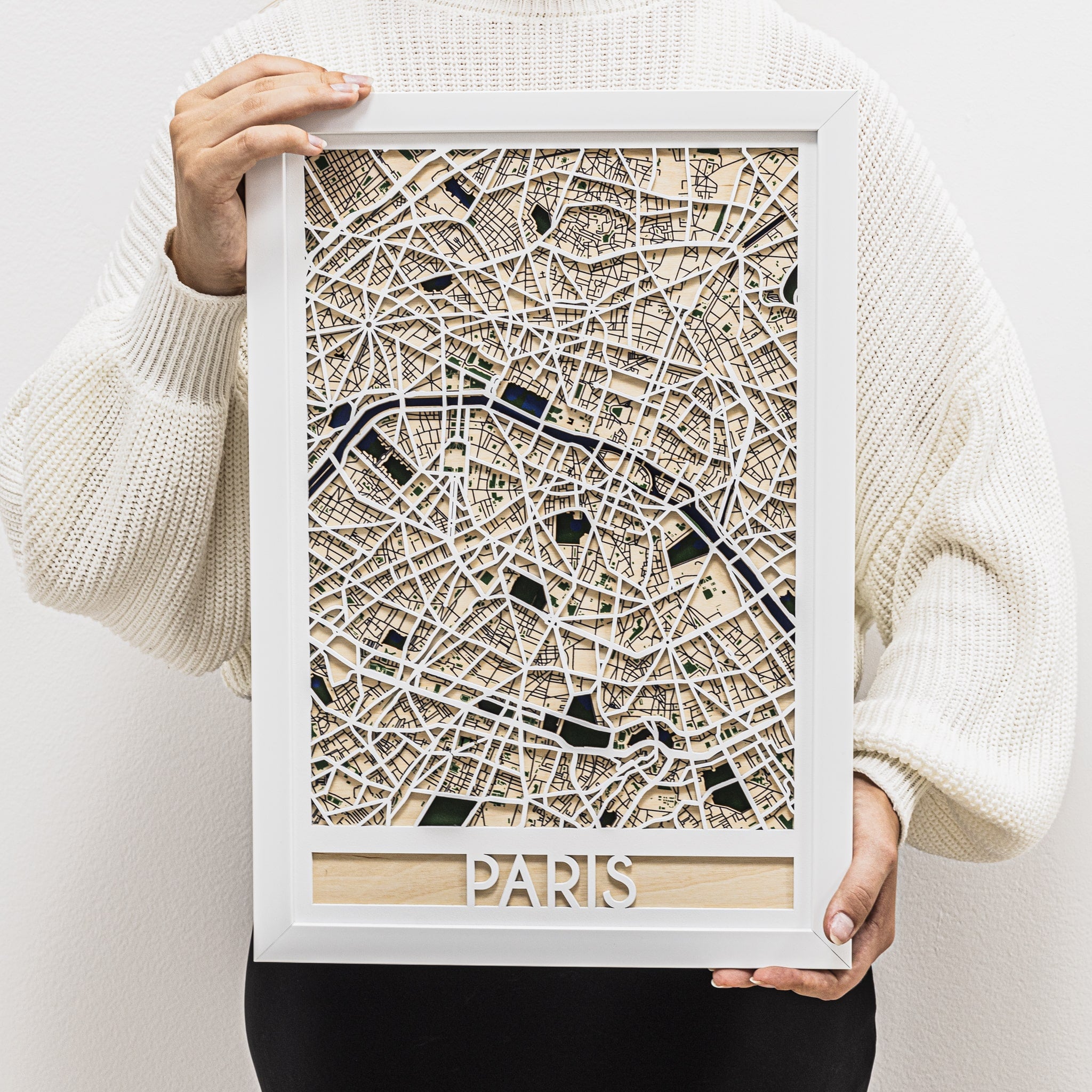 Framed map of Paris held by a person wearing a white sweater.