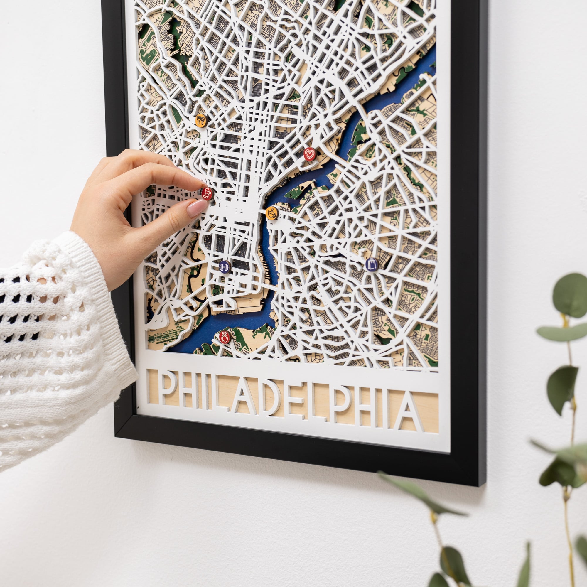 Framed 3D city map of Philadelphia on a white wall with a hand touching it.