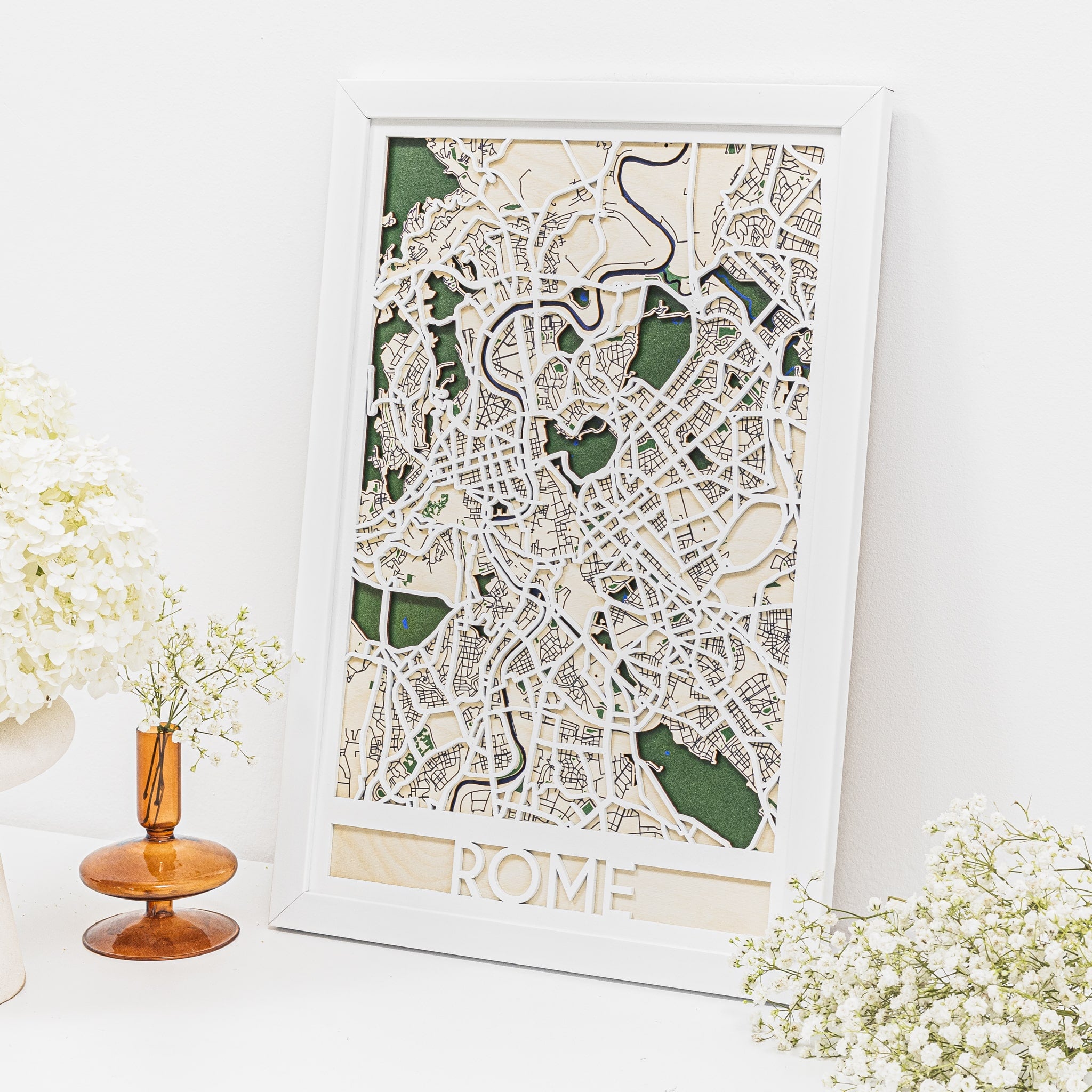 Framed map of Rome on a white wall with decorative flowers.