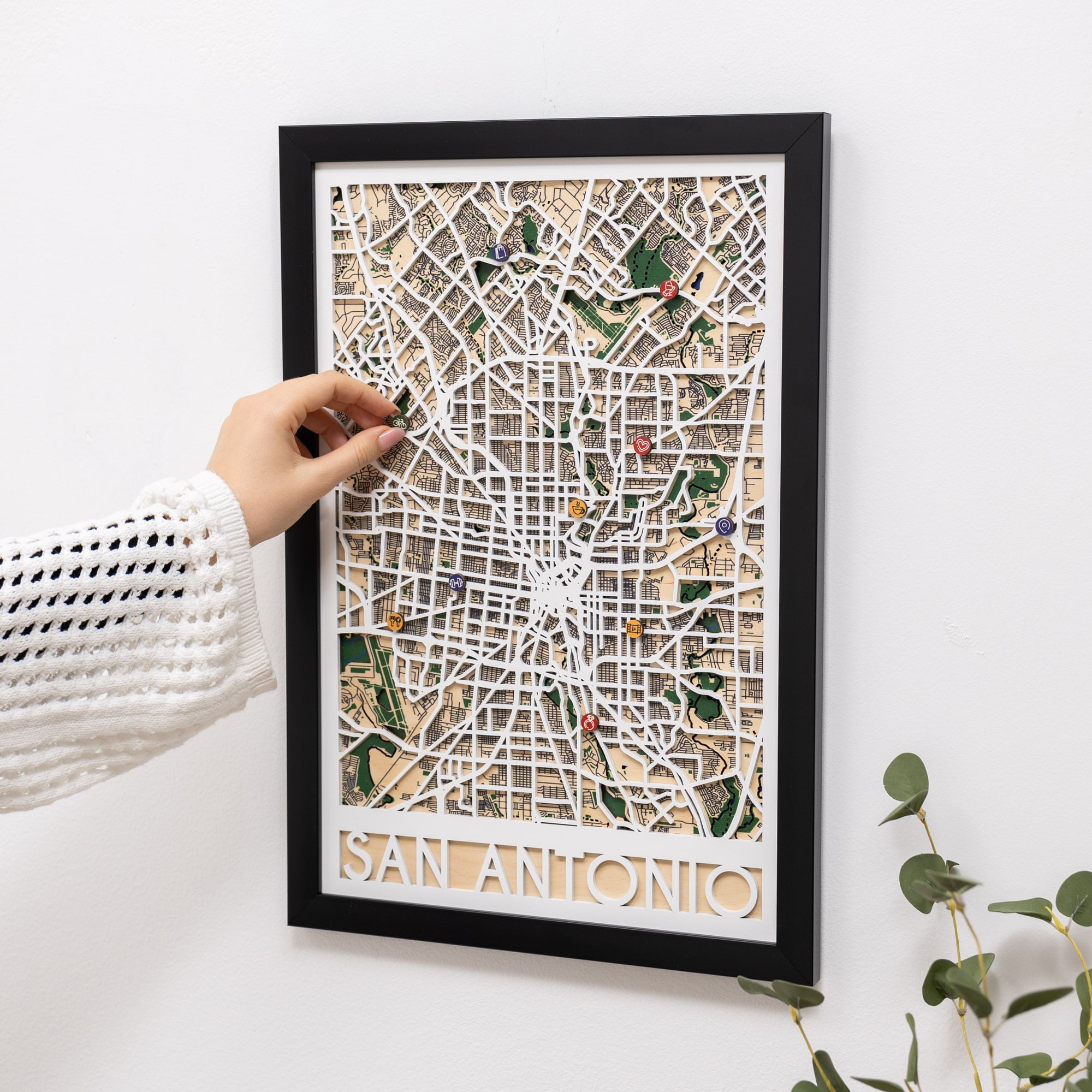 Framed map of San Antonio with decorative pins on a white wall.