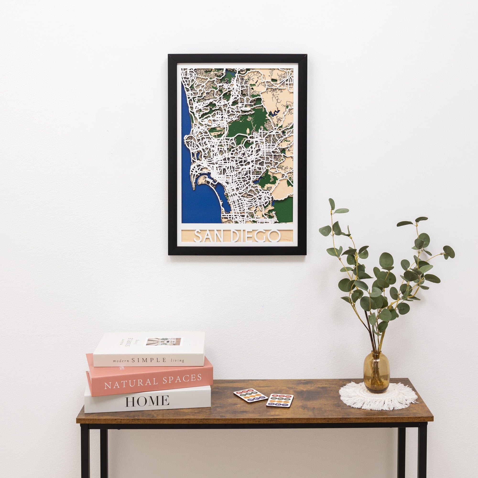 Framed map of San Diego on a wall above a wooden table with books and a plant.