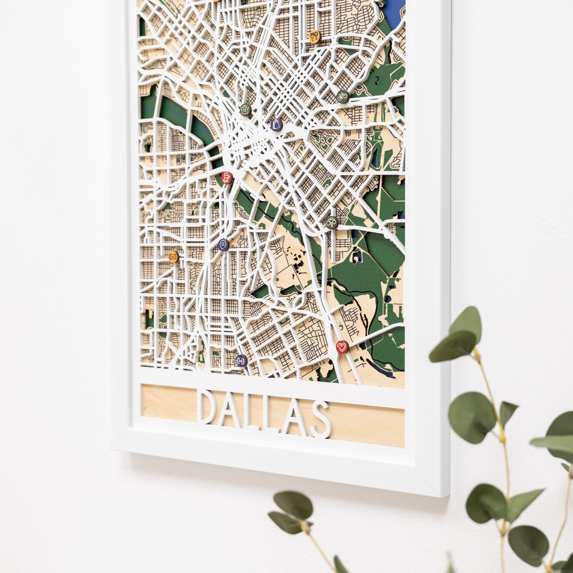 Woman hanging a framed map on a wall next to a wooden side table with books and a plant.