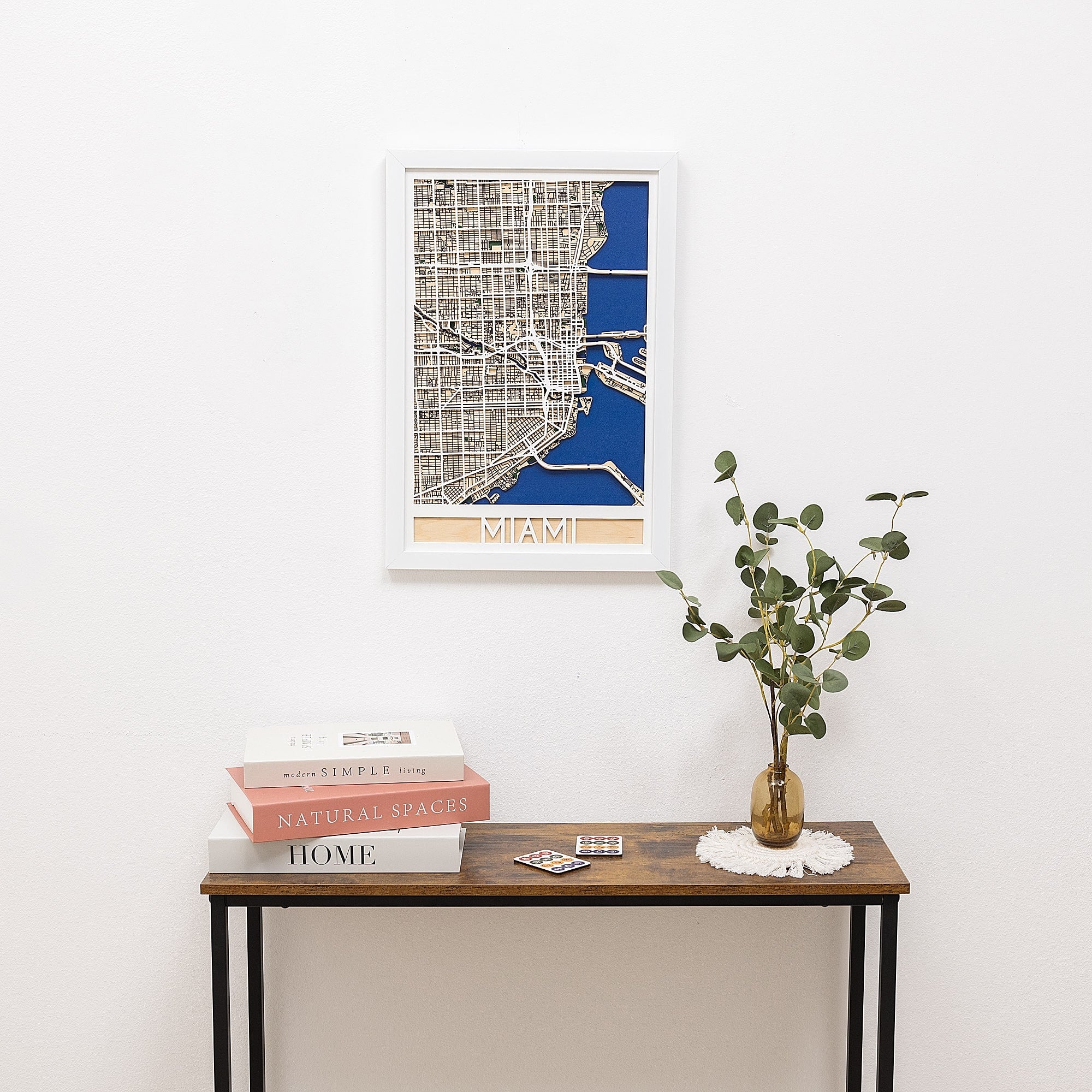 Framed map of Miami on a wall above a wooden table with books and a plant.