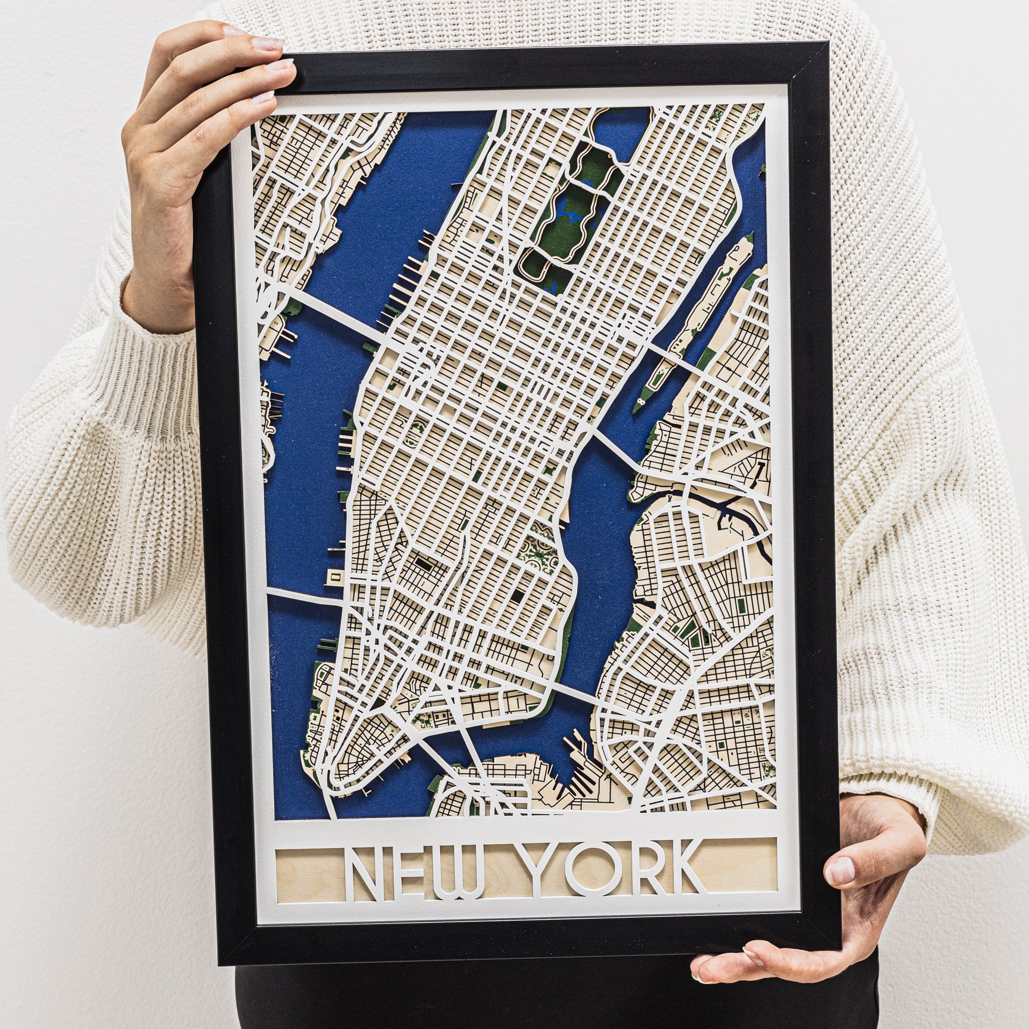 Framed 3D paper model of a city map with 'New York' at the bottom, held by a person.