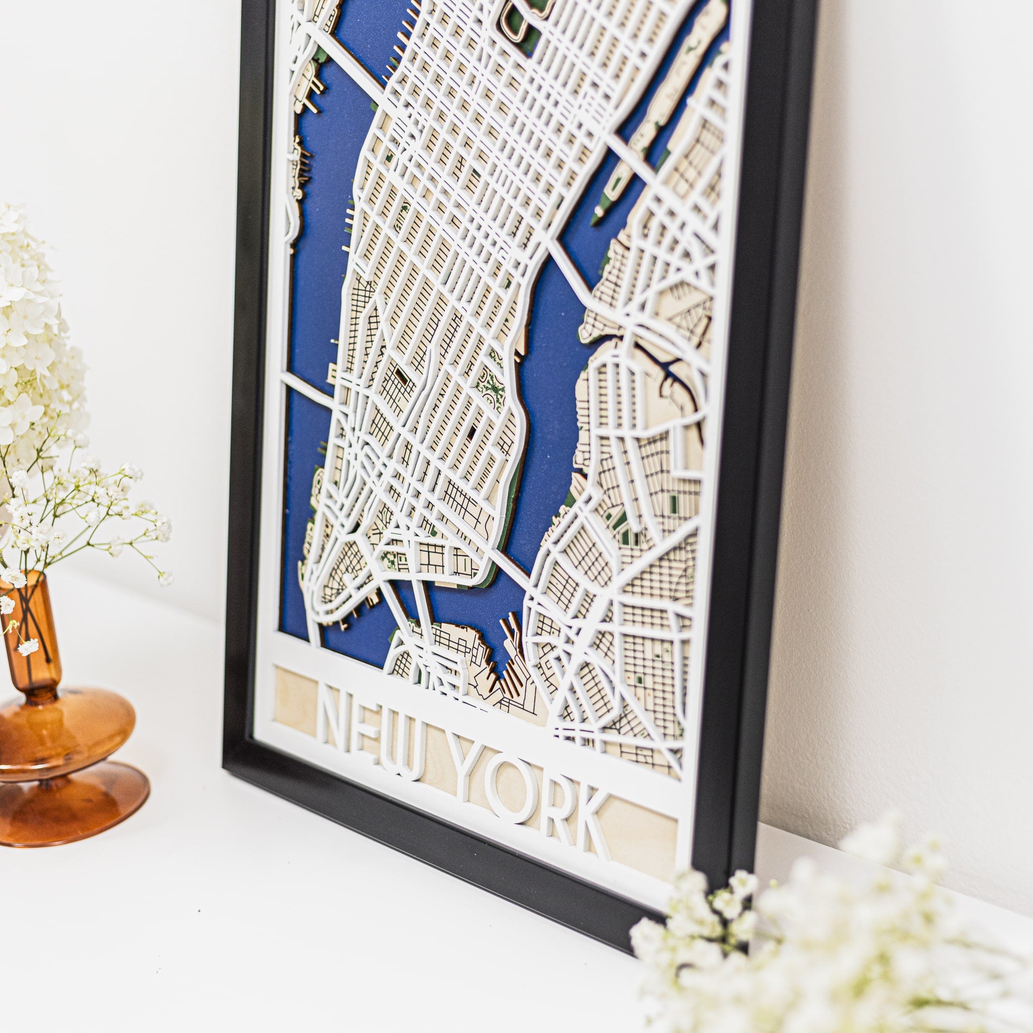 Framed map of New York on a white surface with decorative flowers.