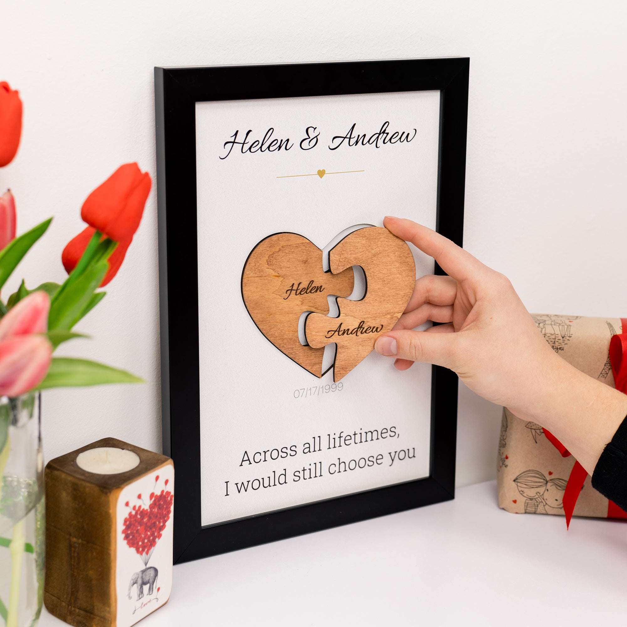 Framed wooden puzzle heart with names 'Helen & Andrew' and romantic quote, held by a hand.