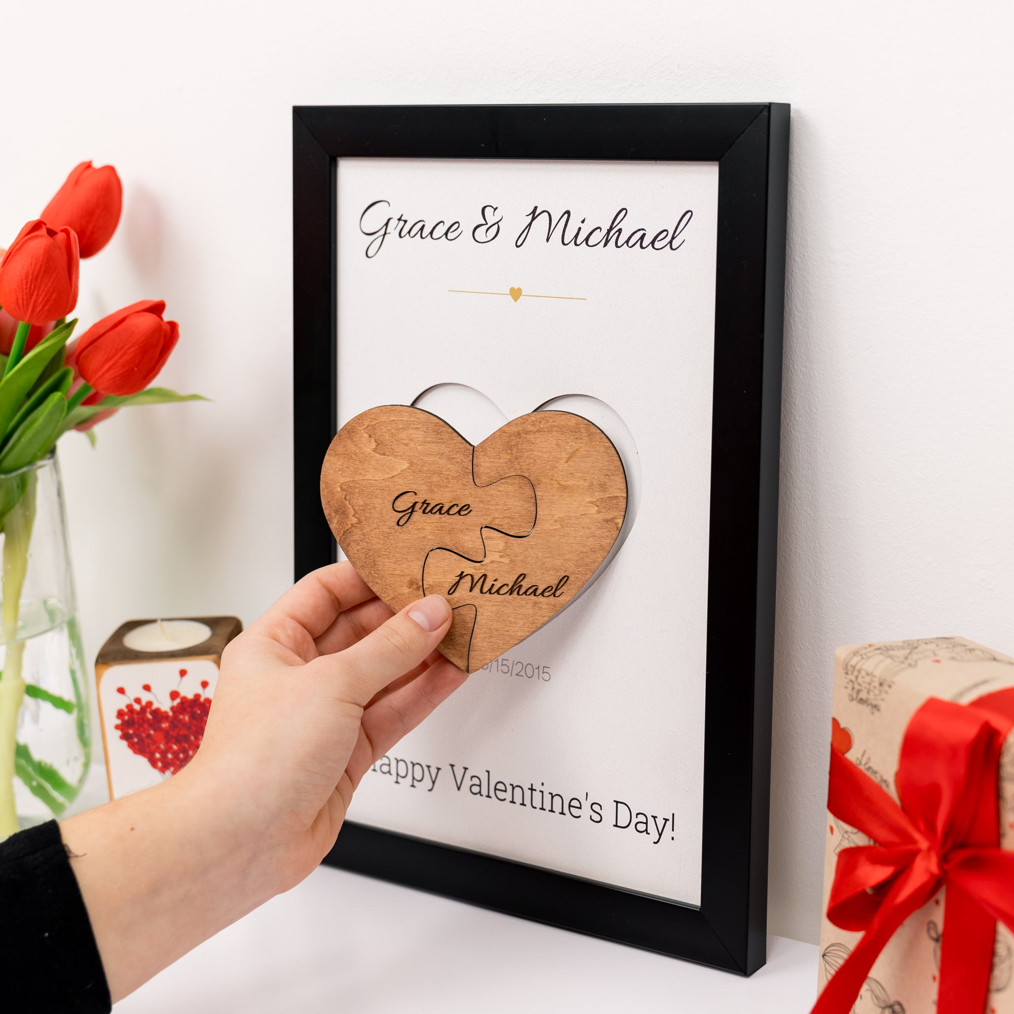 Personalized wooden heart puzzle piece with names in a frame, surrounded by flowers and a gift.