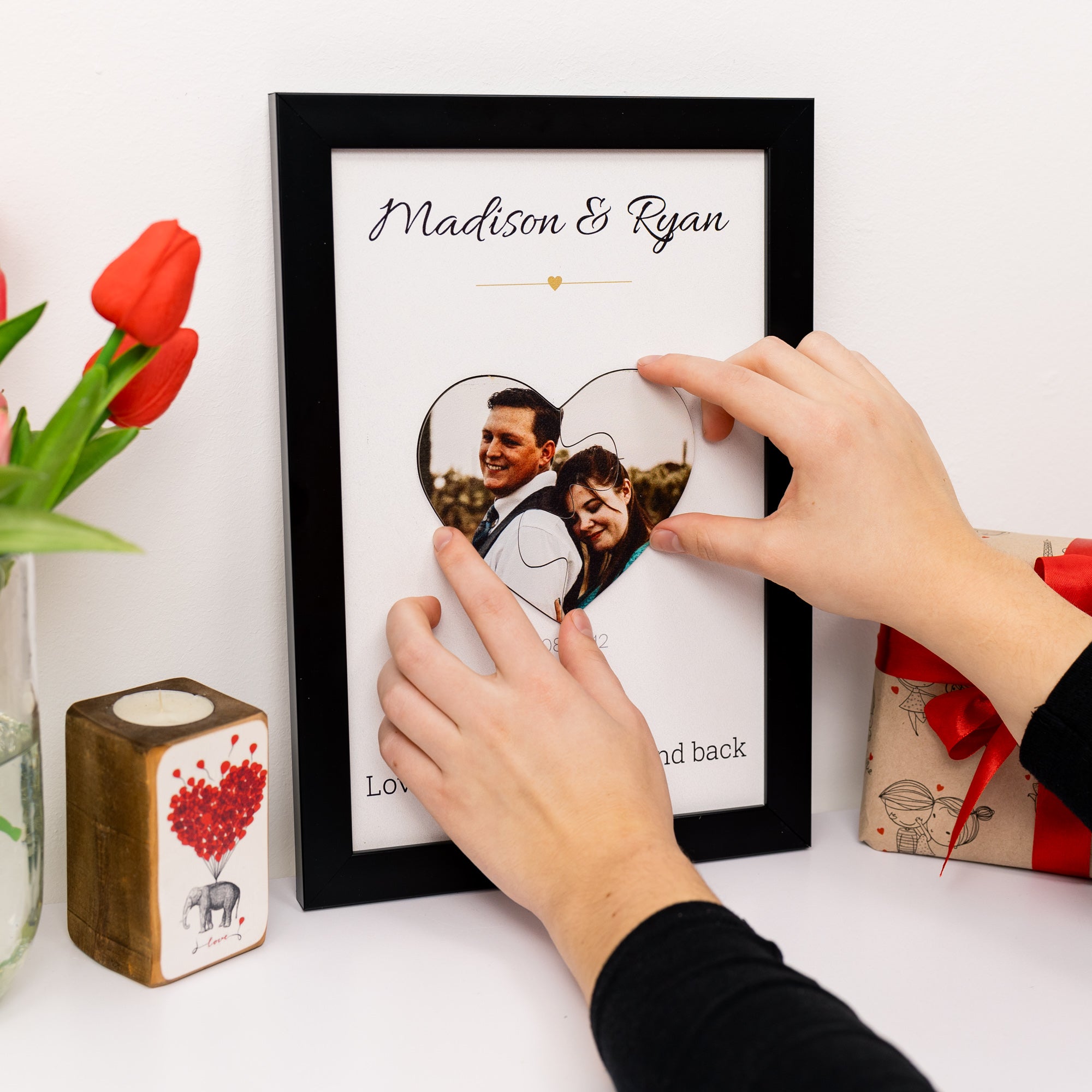 Person adjusting a heart-shaped photo in a framed couple's portrait with 'Madison & Ryan' text.
