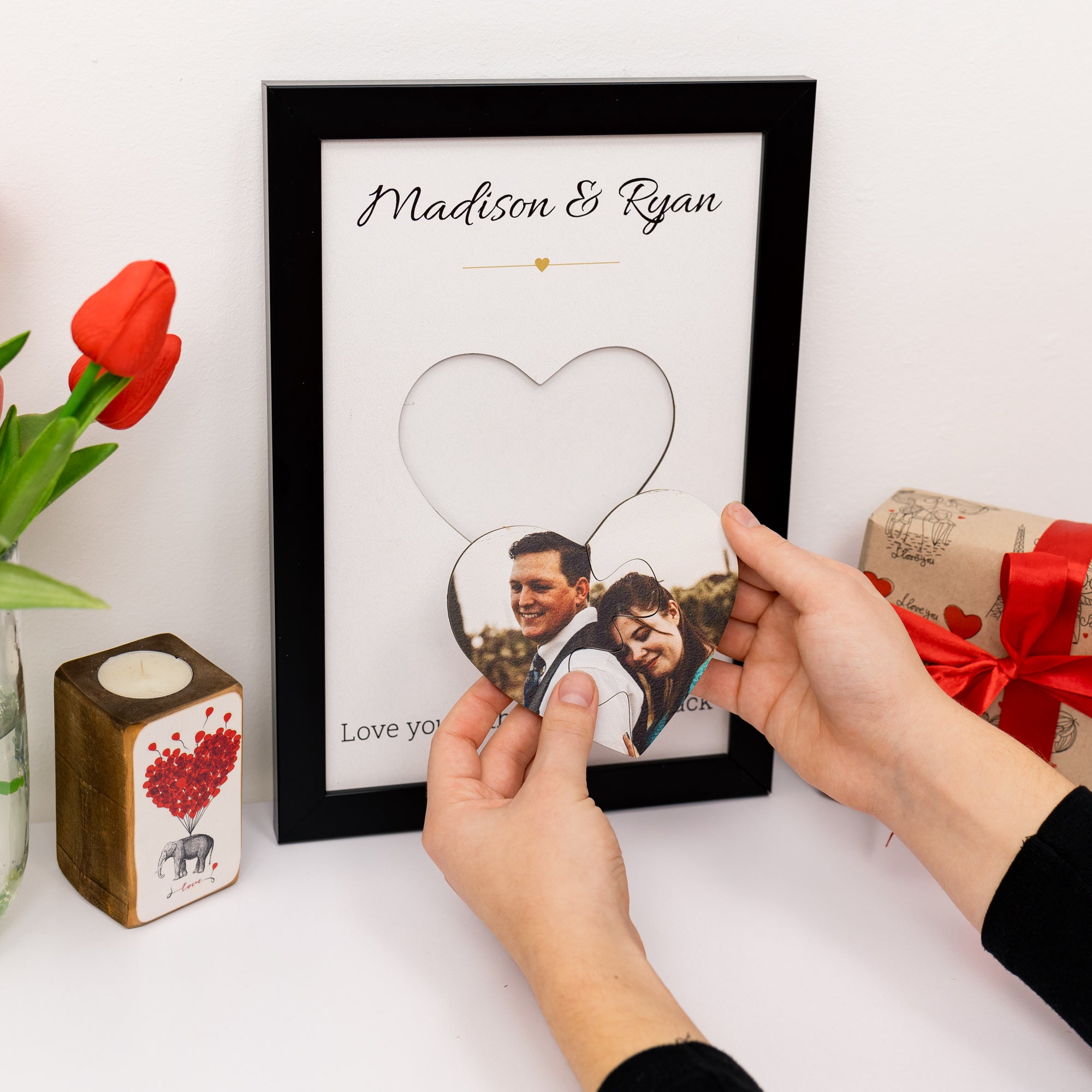 Framed photo of a couple with personalized text, held by a person on a white surface with decorative items.