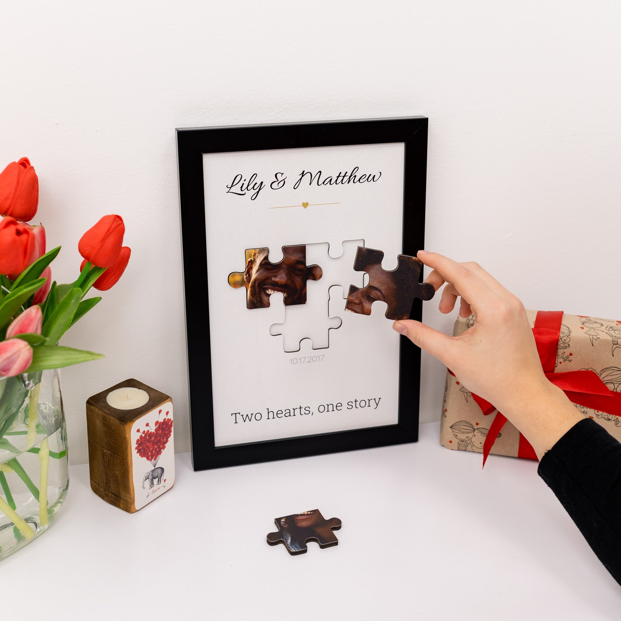 Framed puzzle with 'Lily & Matthew' and 'Two hearts, one story' text, hand placing a puzzle piece.