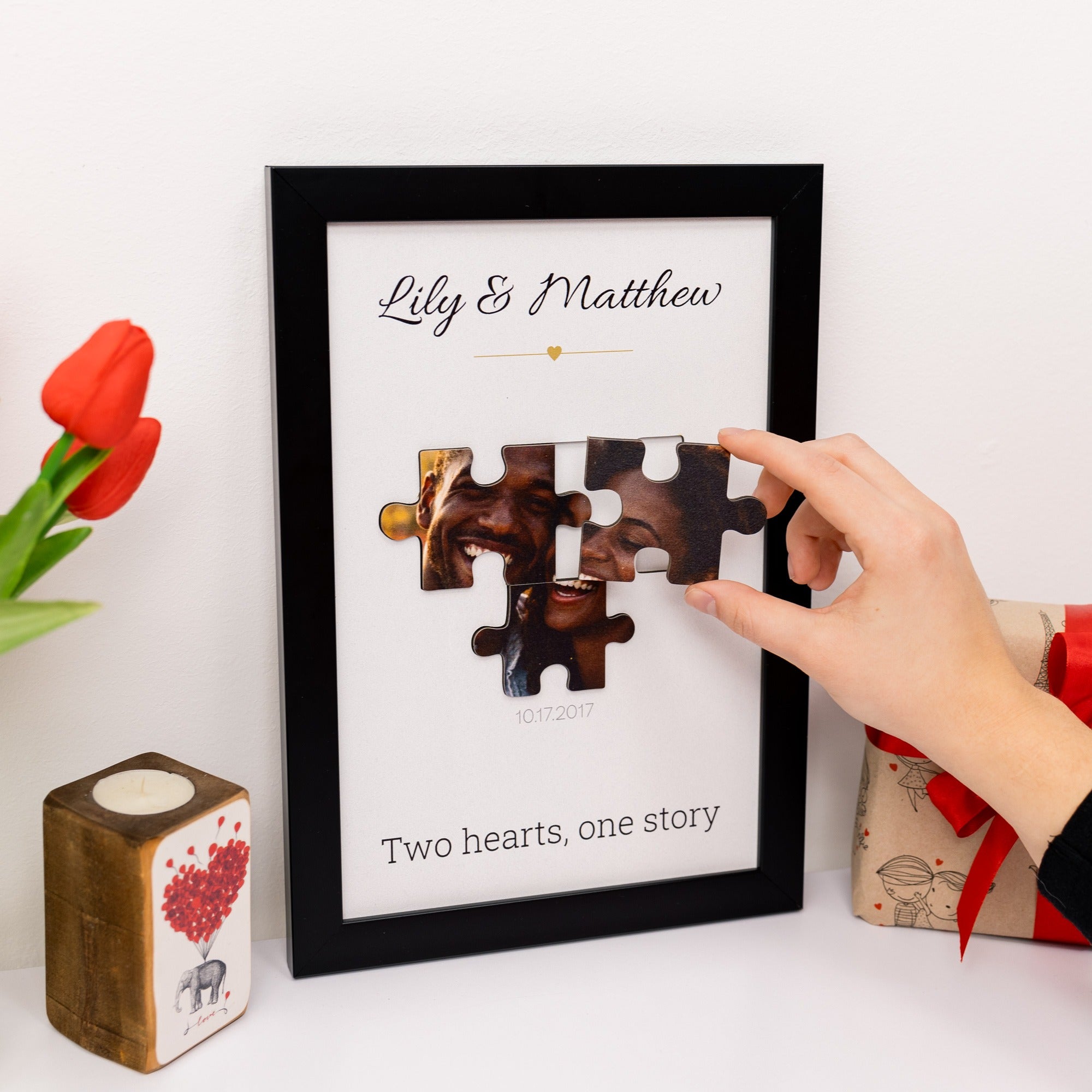 Framed puzzle piece art with 'Lily & Matthew' and 'Two hearts, one story' text, hand pointing at it.
