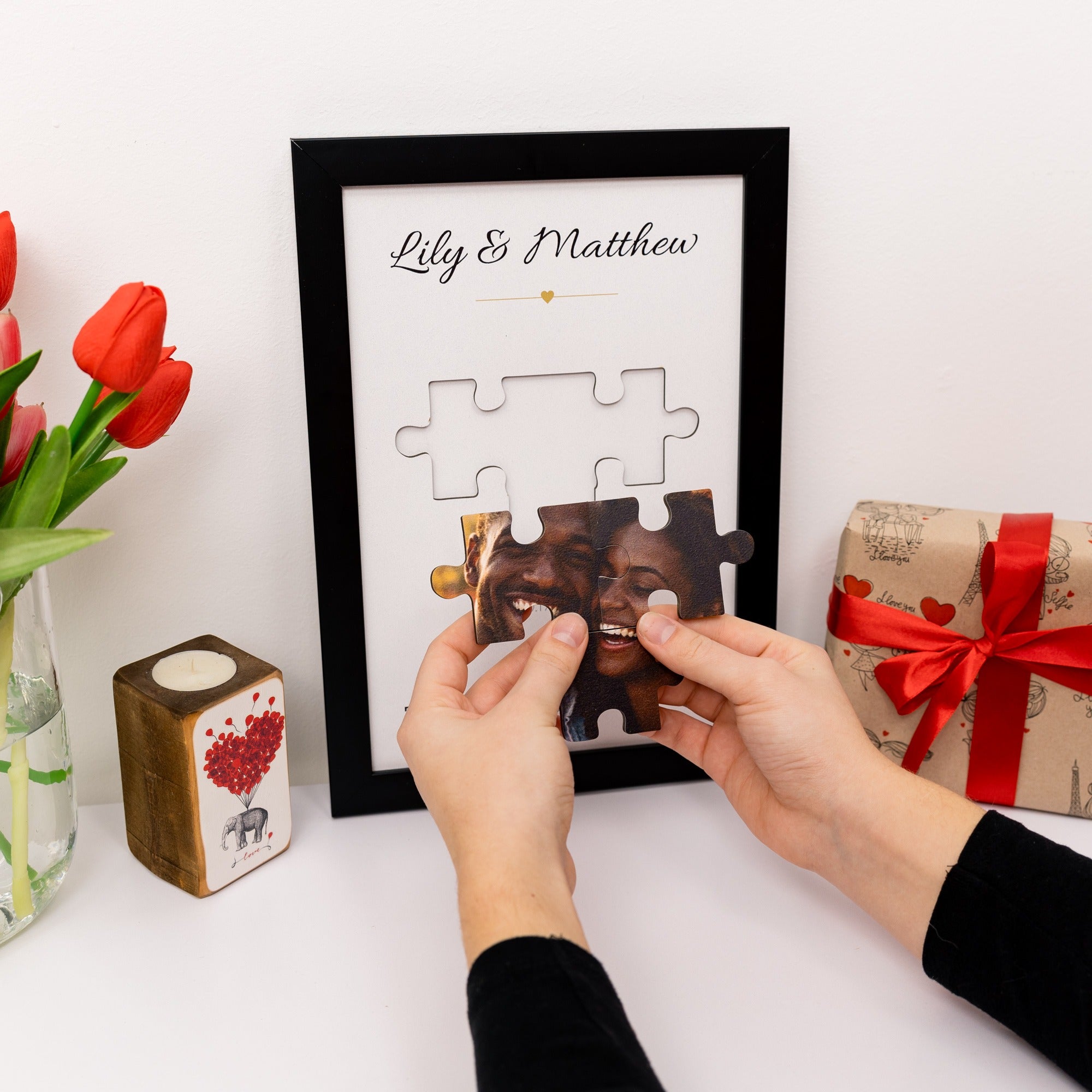 Personalized photo puzzle framed with a couple's name, surrounded by decorative items on a white surface.