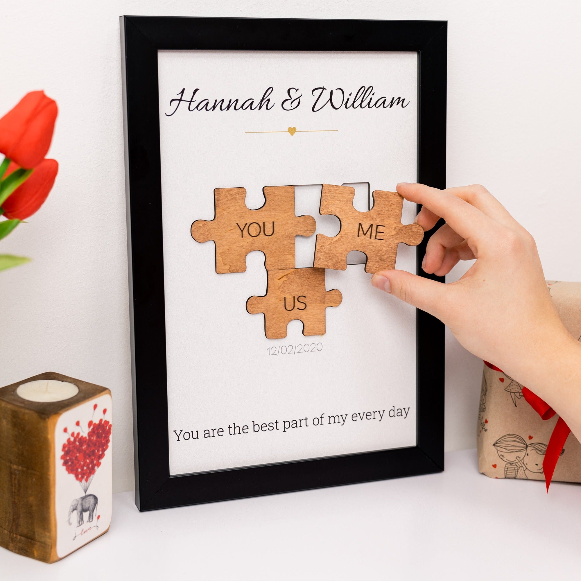 Framed wooden puzzle pieces with 'YOU' and 'ME' on a white background, held by a hand.