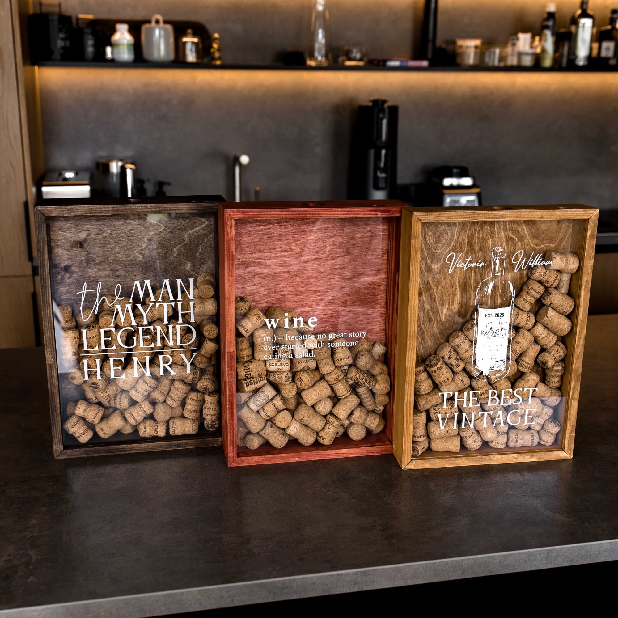 Three wooden wine-themed shadow boxes displayed on a dark countertop. The left box is dark brown with white text reading 'the MAN MY TH LEGEND HENRY' and shows corked wine bottles.