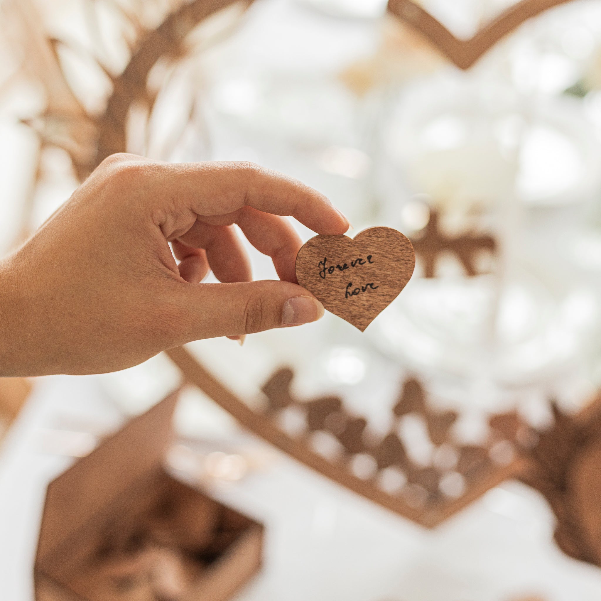 Hand holding a wooden heart with 'Forever love' engraving against a blurred background