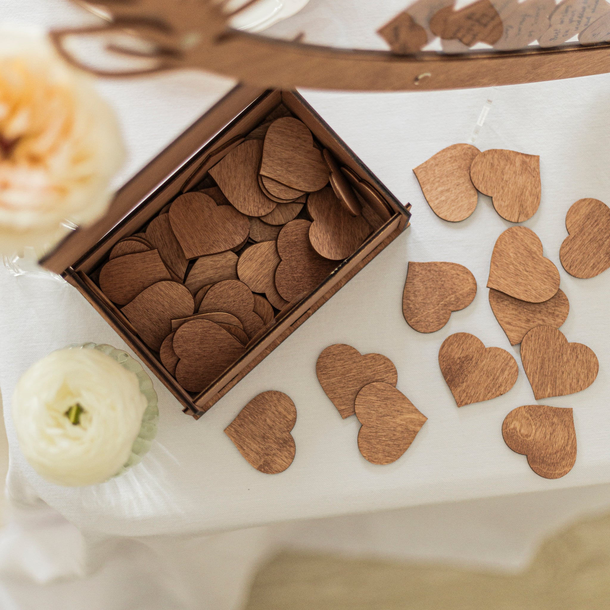 Wooden heart-shaped confetti on a white surface with a box of confetti.