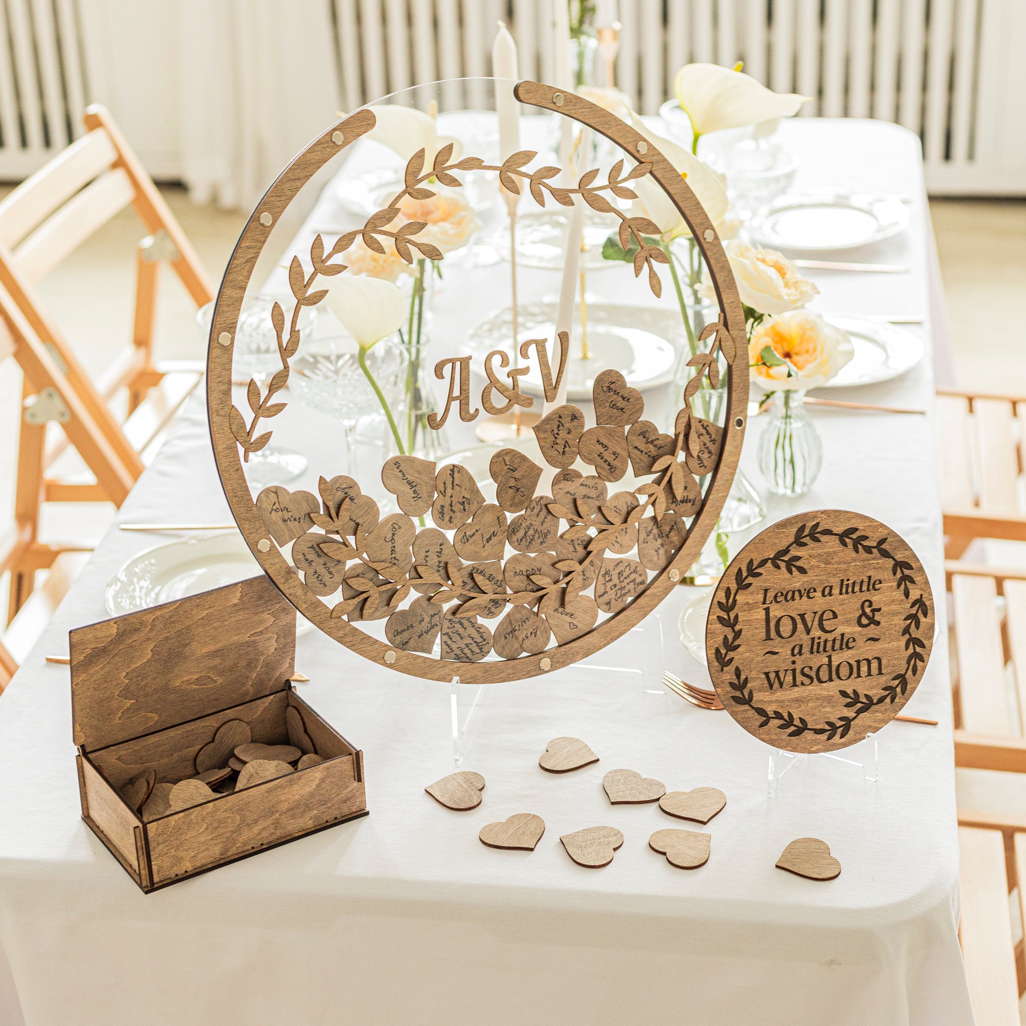 Wooden wedding centerpiece with 'A&V' initials, heart-shaped wooden pieces, and a small box on a table.