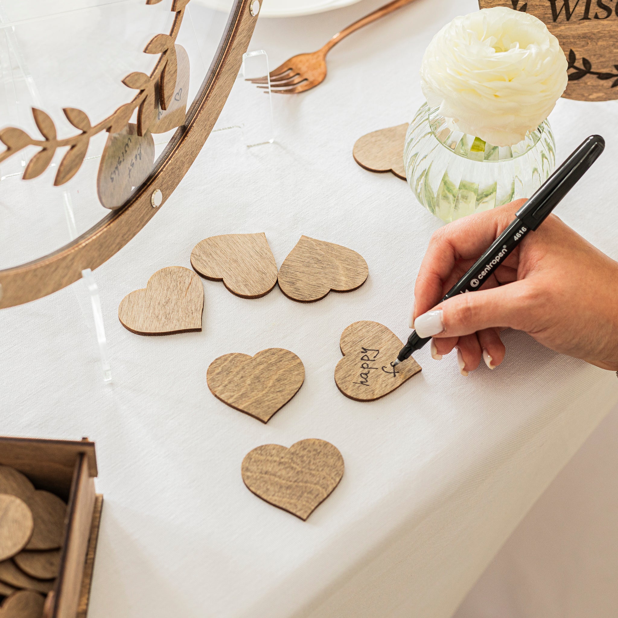 Hand writing on wooden heart-shaped pieces with a pen, surrounded by decorative items.