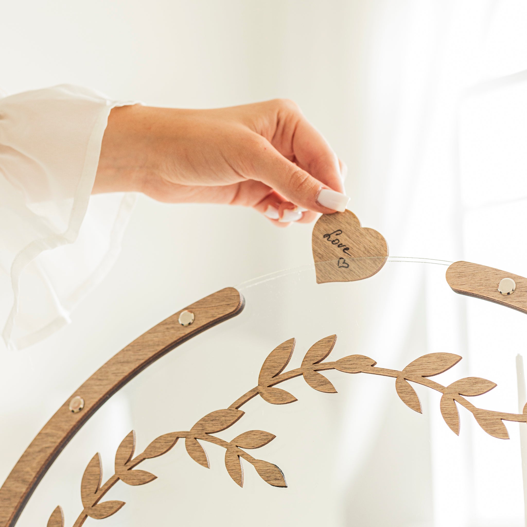 Hand holding a heart-shaped tag with 'love' written on it, attached to a decorative wreath.