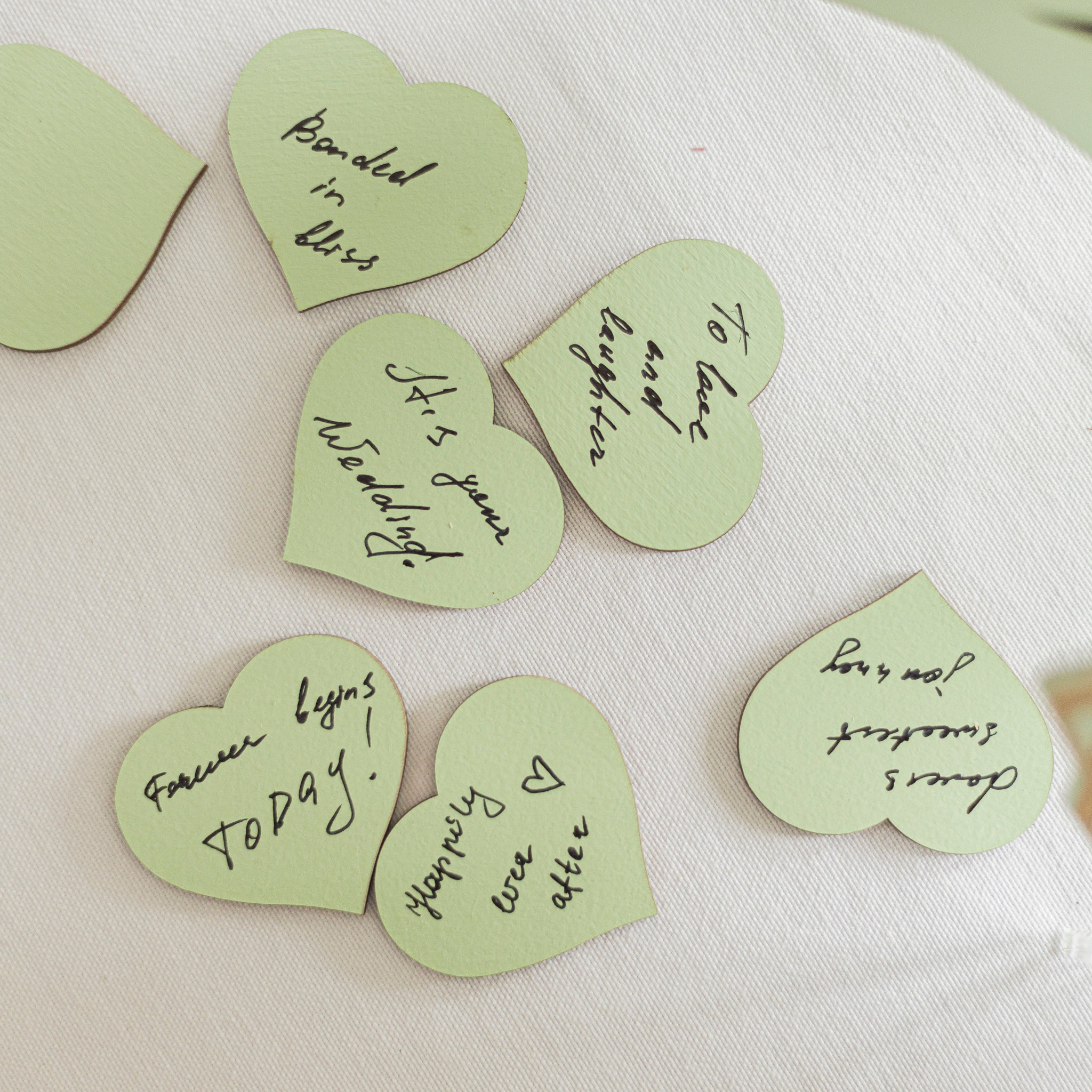 Green heart-shaped cards with handwritten messages on a white fabric background