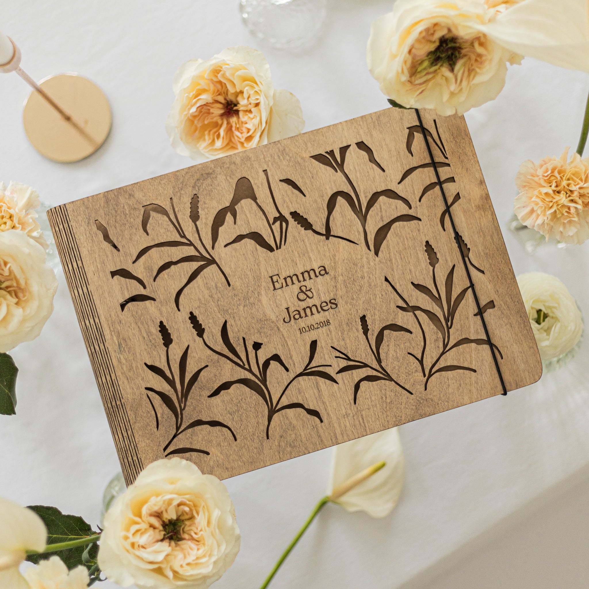 Personalized wooden book with floral design and 'Emma & James' engraving, surrounded by white flowers.