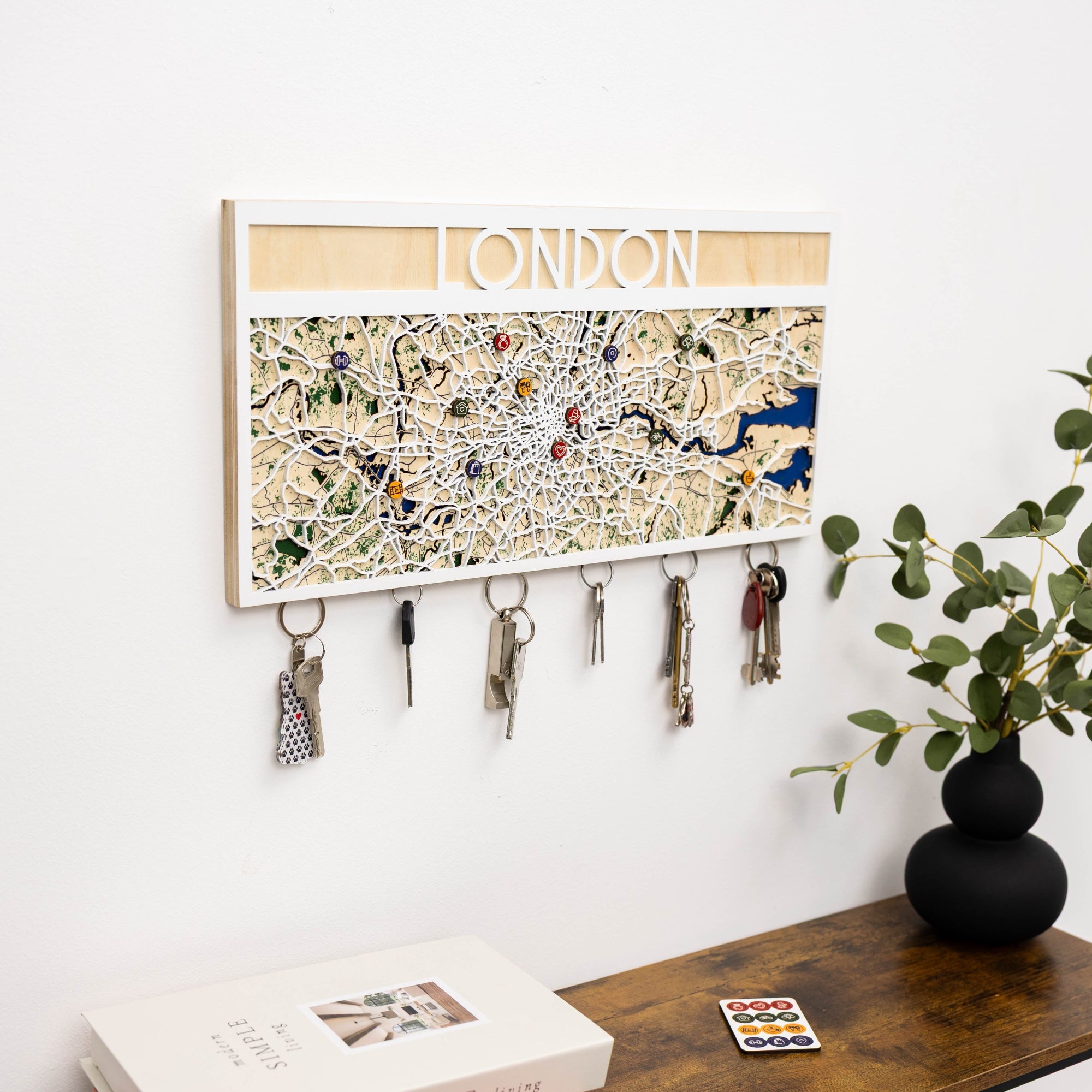 Key holder with London map design on a wall above a desk with a plant and books.
