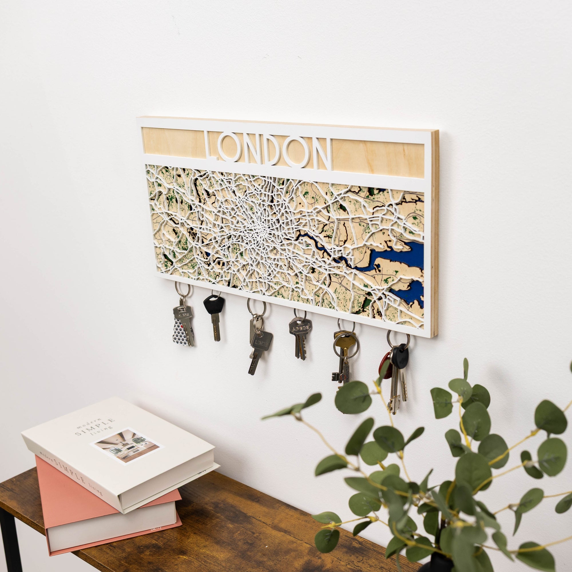 Key holder with London map design on a white wall, next to a wooden bench and books.