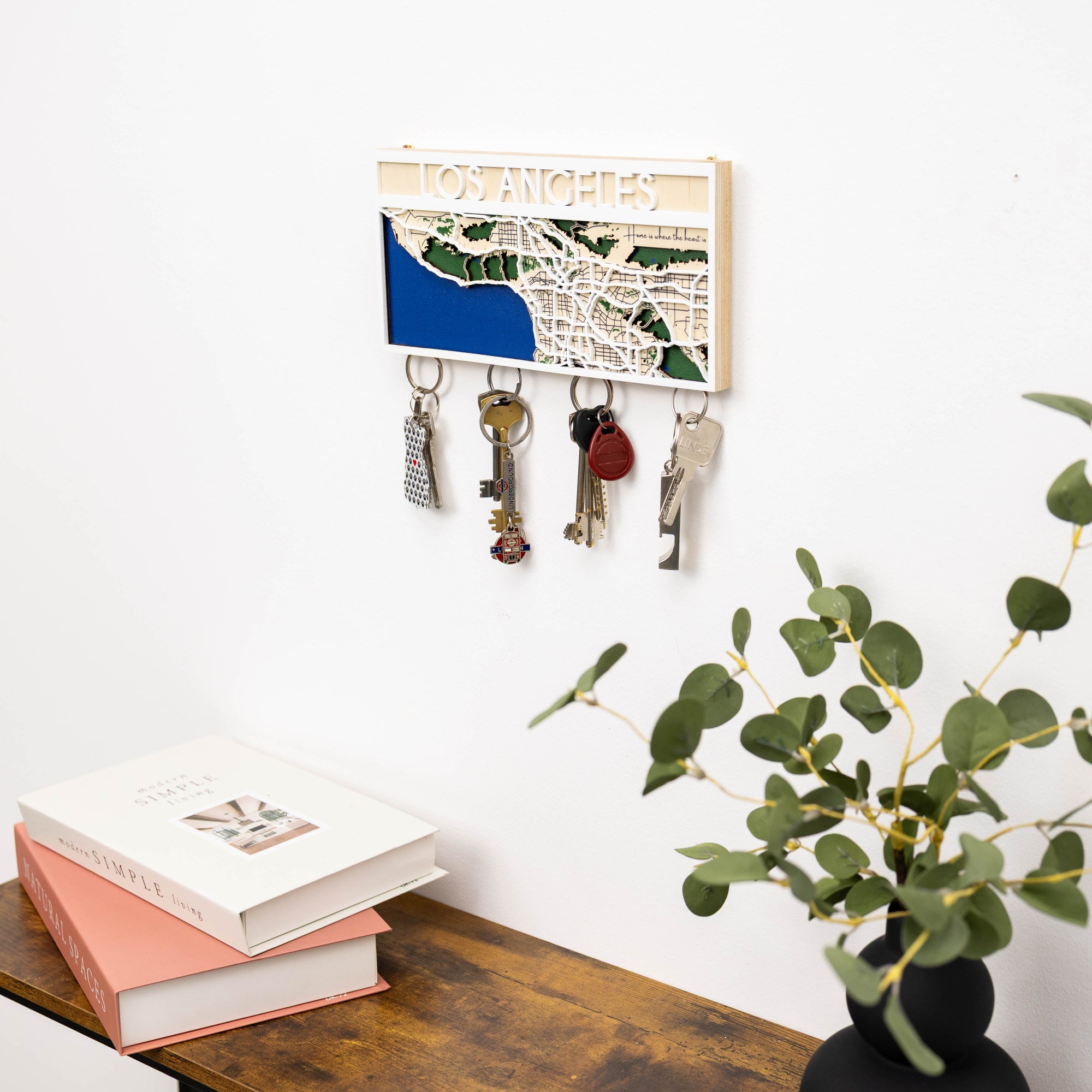 Key holder with keys on a wall above a desk with books and a plant.
