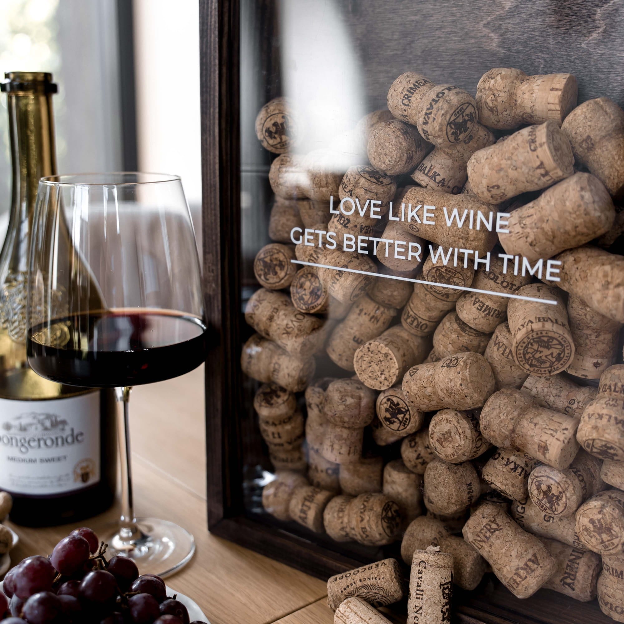 A framed wall art piece filled with wine corks, with a glass of red wine